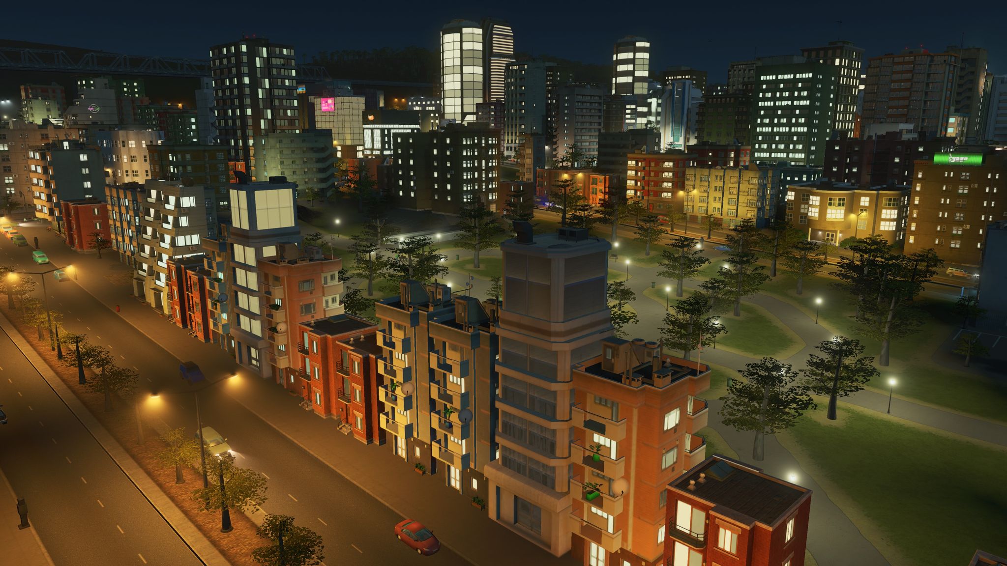 A screenshot from Cities: Skylines on Xbox One of a nighttime view of one of my cities. It has a big park with lots of paths through it surrounded by small unit blocks, with larger and taller unit blocks over the other side of the park in the distance.