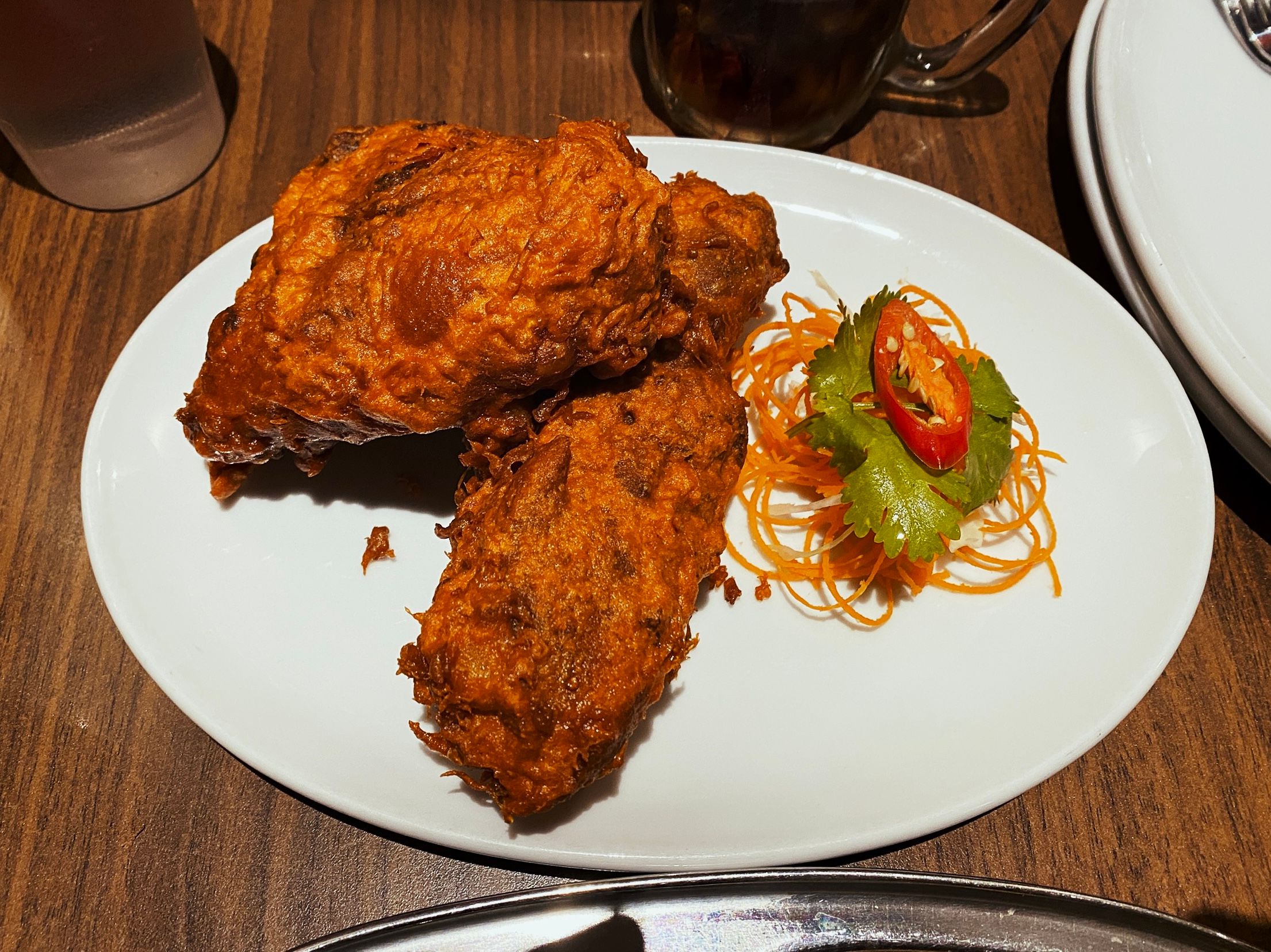 A photo of two pieces of fried chicken on a plate. They're a rich dark red/brown colour.