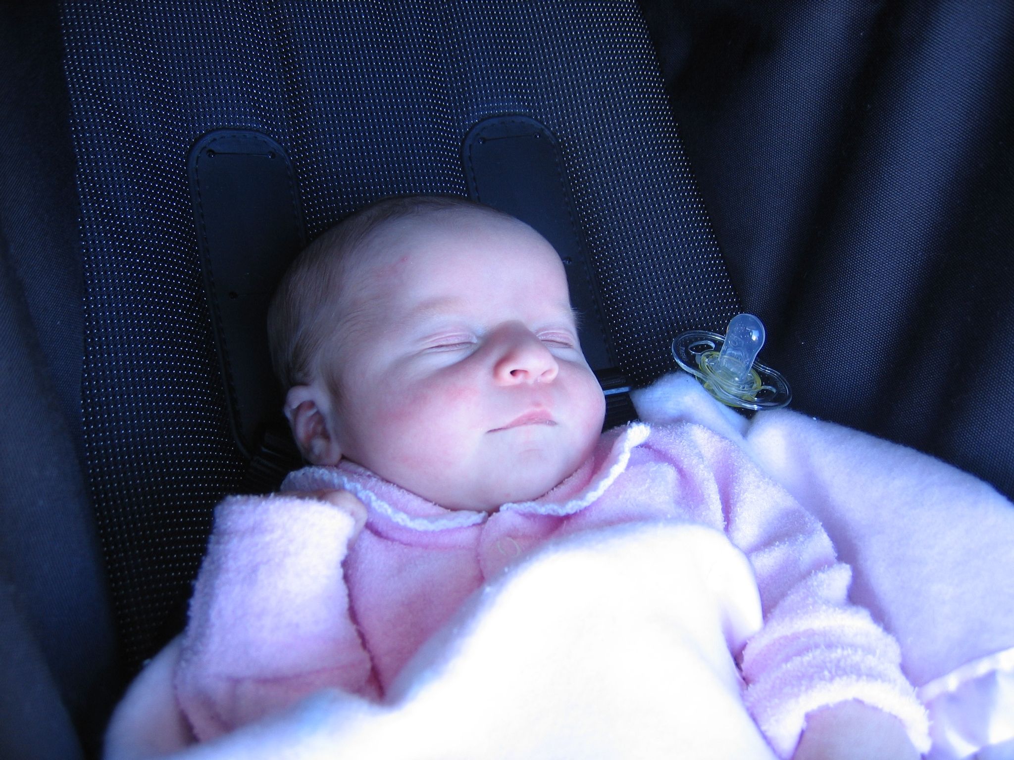 A photo of a newborn baby all clothed and wrapped up in pink, lying asleep in a stroller.