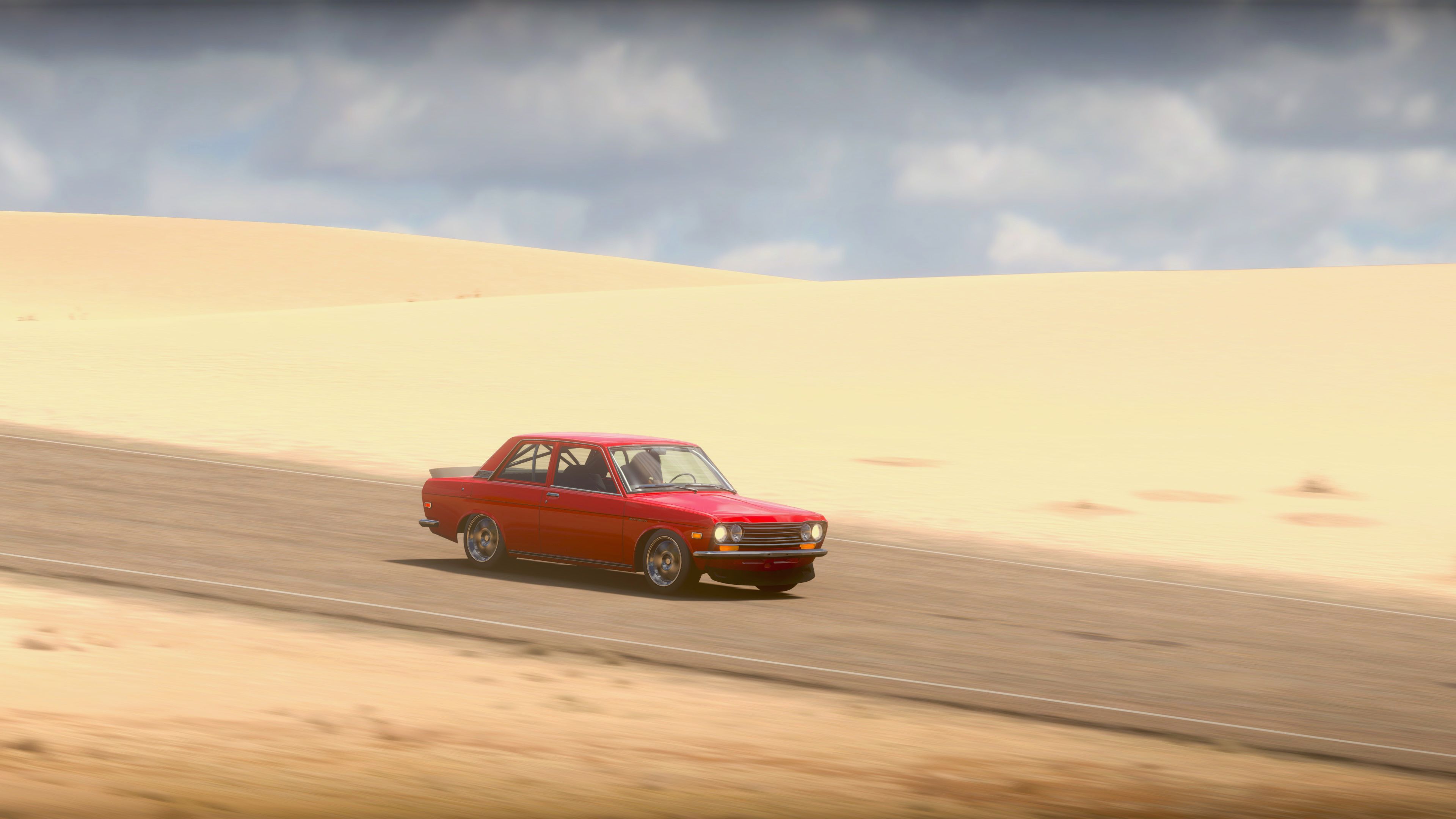 A screenshot showing a hotted-up (pun unintended) red 1970 Datsun 510 driving along a road with rolling sand dunes behind it and clouds in the distance, and the sun blazing down. Just looking at it, it feels HOT.