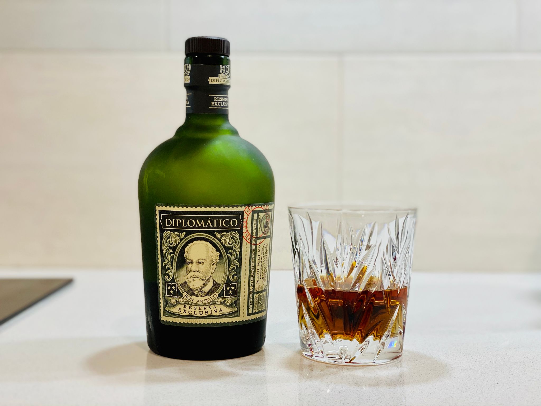 A photo of a bottle of Diplomatico rum next to a lead crystal glass with some of the rum in it.
