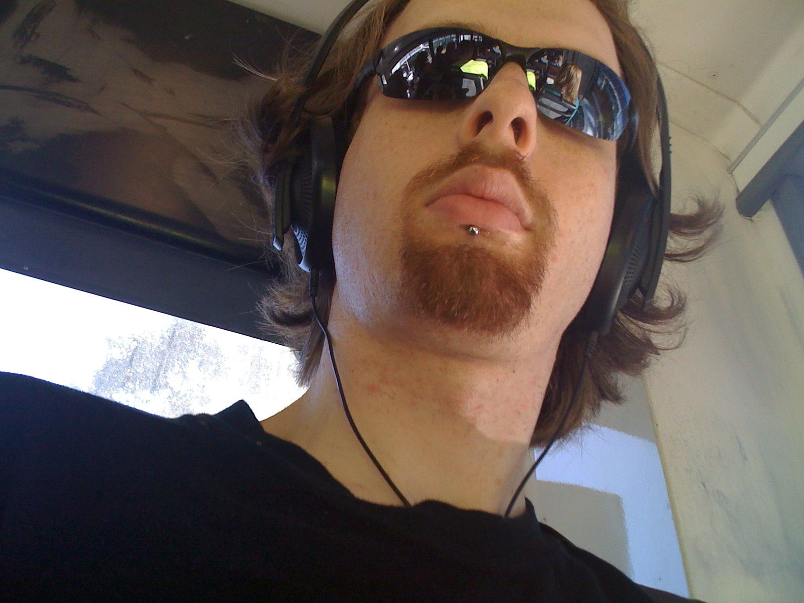 A selfie of me, a white man with not-quite-shoulder-length brown hair and a short nicely-trimmed red goatee. I'm wearing sunglasses and have big headphones on.