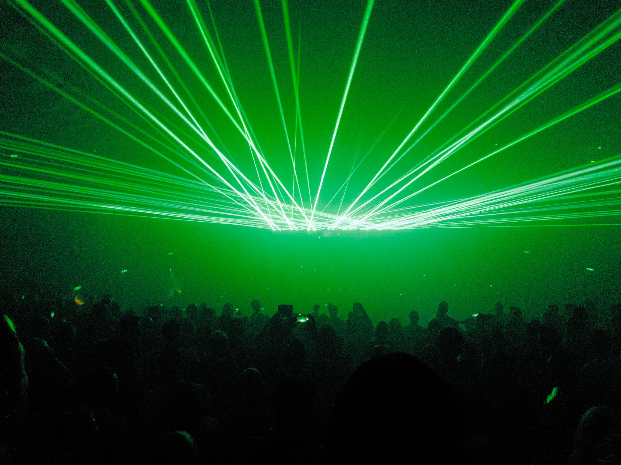 Many bright green lasers shooting out from the stage above the point of view of the photo, with the crowd visible at the bottom in an eerie green glow.