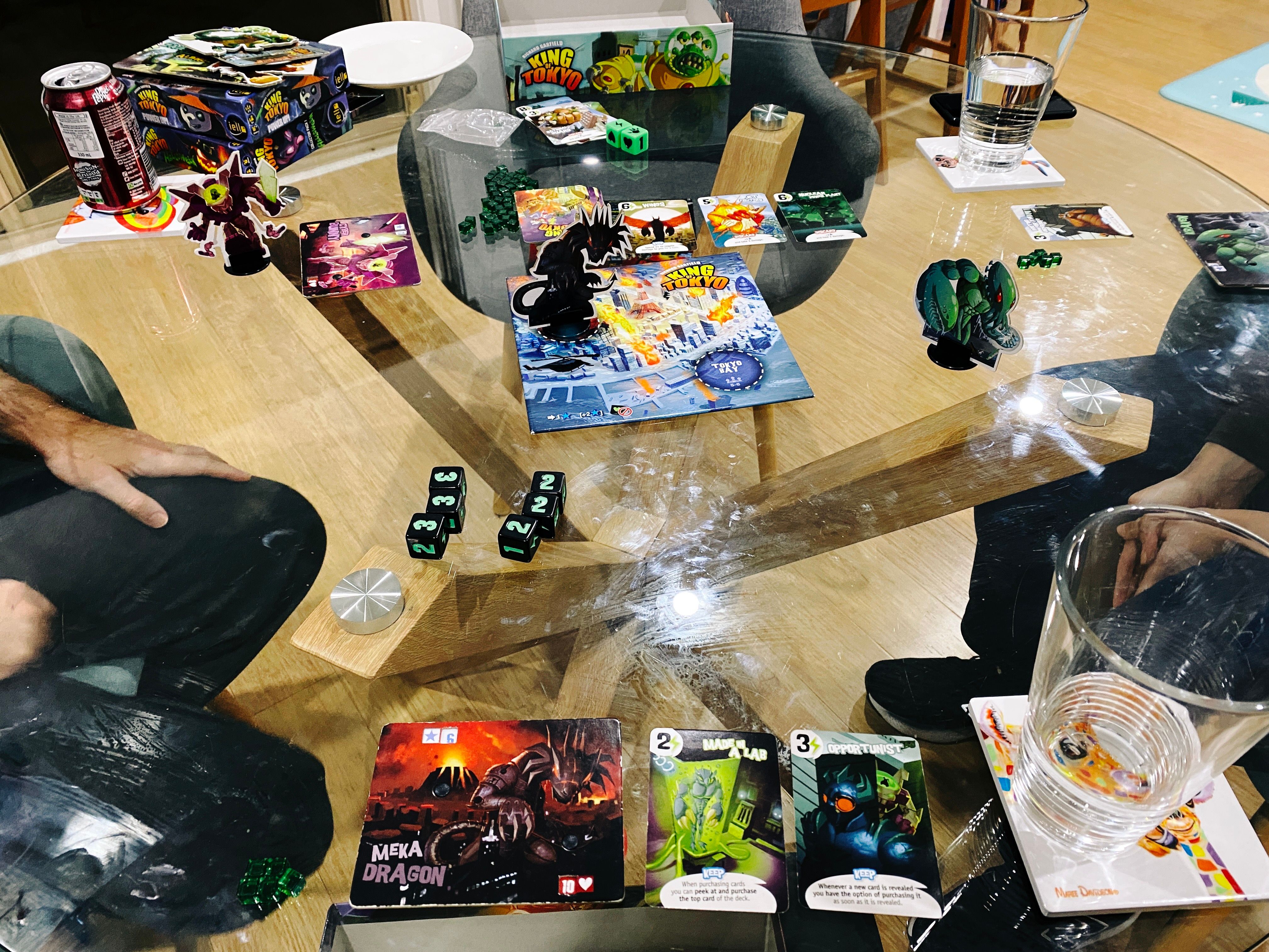 A photo of a game of King of Tokyo. This is much less involved, there's three cutouts of monsters standing upright and a small board with a cartoon version of the coastline of Tokyo and its buildings, plus a number of cards with cartoony artwork on them.