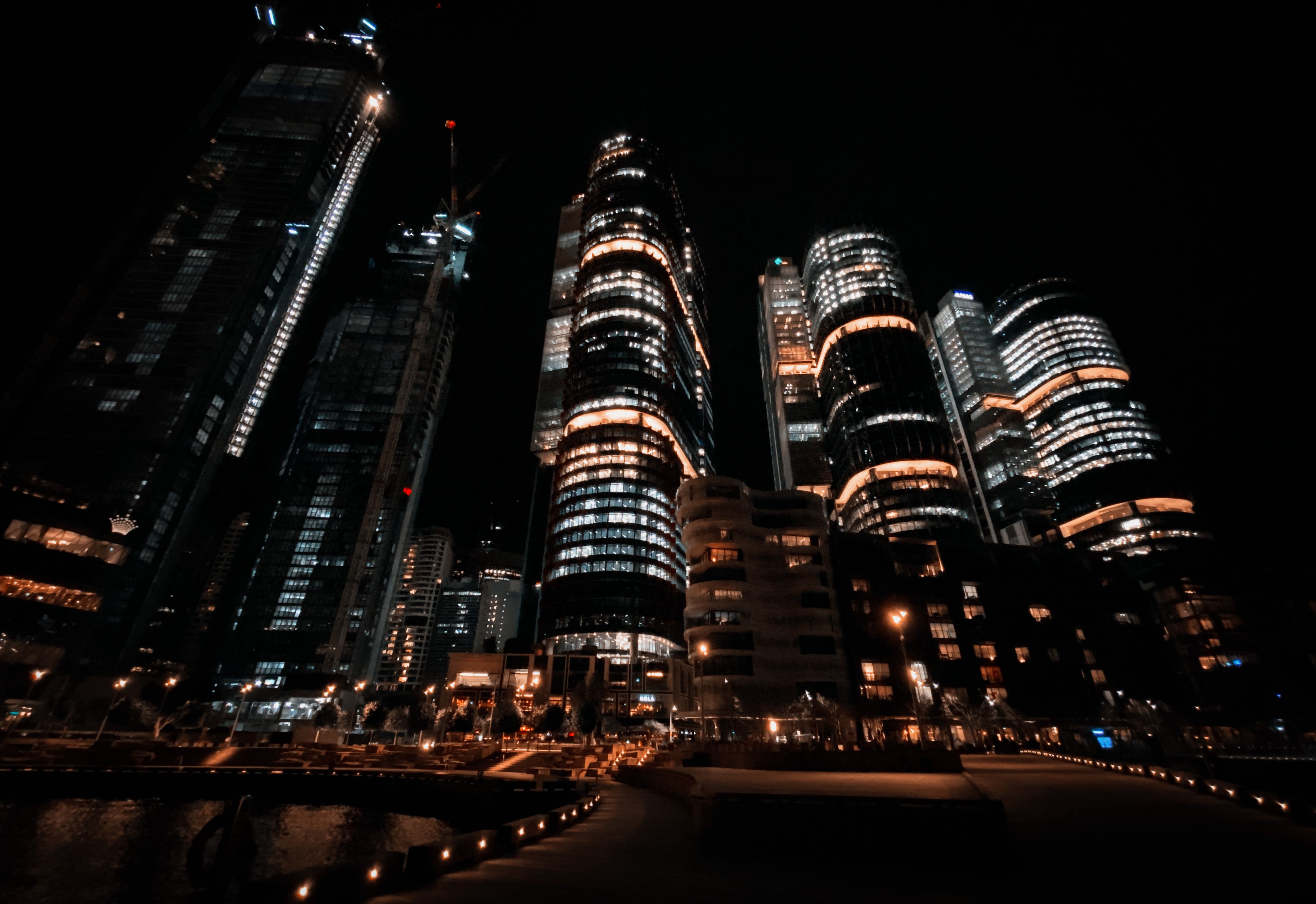 A photo taken at night looking up at three huge tower buildings. The front of them are curved and the lights are mostly blue but with a couple of sections where it's a much warmer, yellow colour. The photo itself is slightly blurry which makes it almost look like it's looking up into clouds which makes the buildings seem even taller.