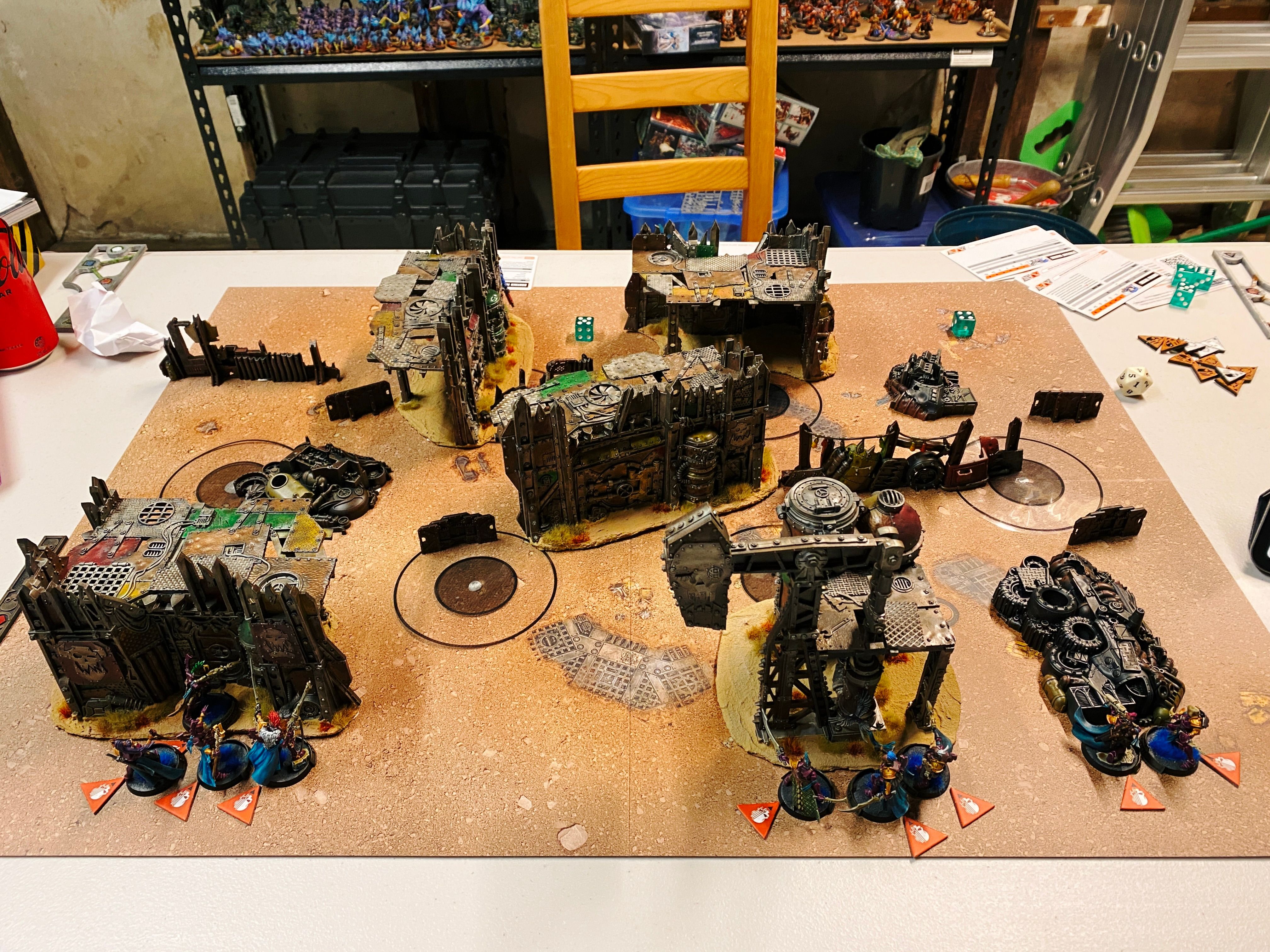 A photo of the board at the start of a game of Warhammer 40,000: Kill Team. The terrain is Ork-style and the structures look like like a junkyard and are very ramshackle. Closest to the camera are my Coirsair Voidscarred, basically lithe space elves in fuchsia armour and turquoise cloaks. I was facing Space Marines but you can't see them in the photo because they're all in cover and not visible from this point.