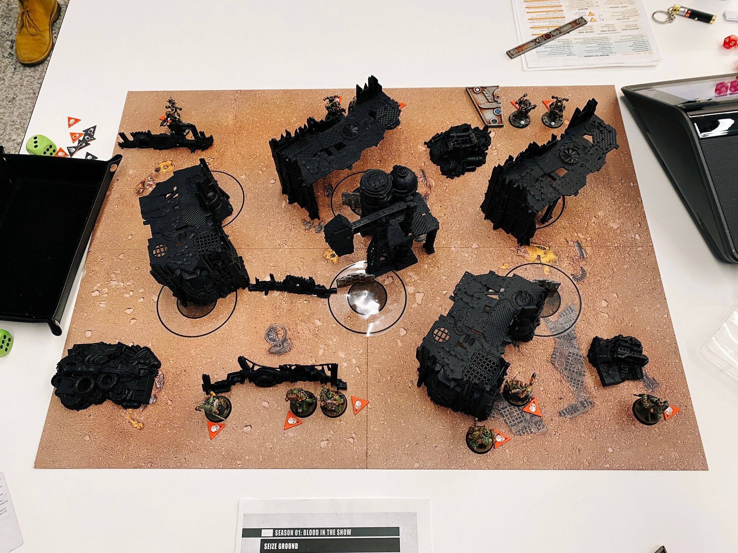 A photo of a Warhammer 40,000 game board, with painted miniatures and shamefully unpainted terrain that looks like a junkyard on it. (...the terrain itself looks like a junkyard, the fact that it's shamefully unpainted is unrelated to this.)