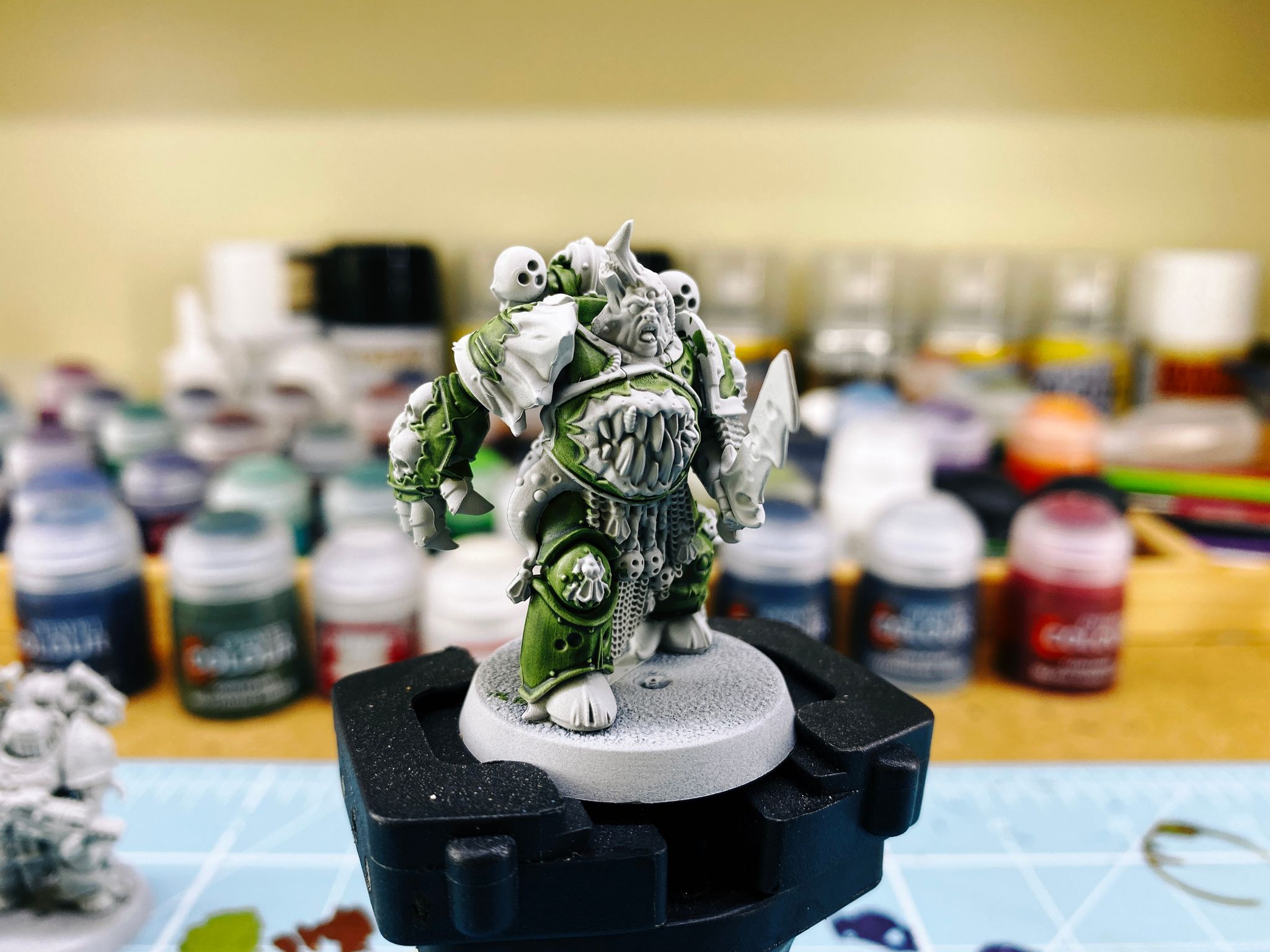 A photo of a partially painted Plague Marine from Warhammer 40,000. He's got tentacles coming out from various armour gaps, a giant mouth with teeth in it in his abdomen, and a bone spike coming out of his head.
