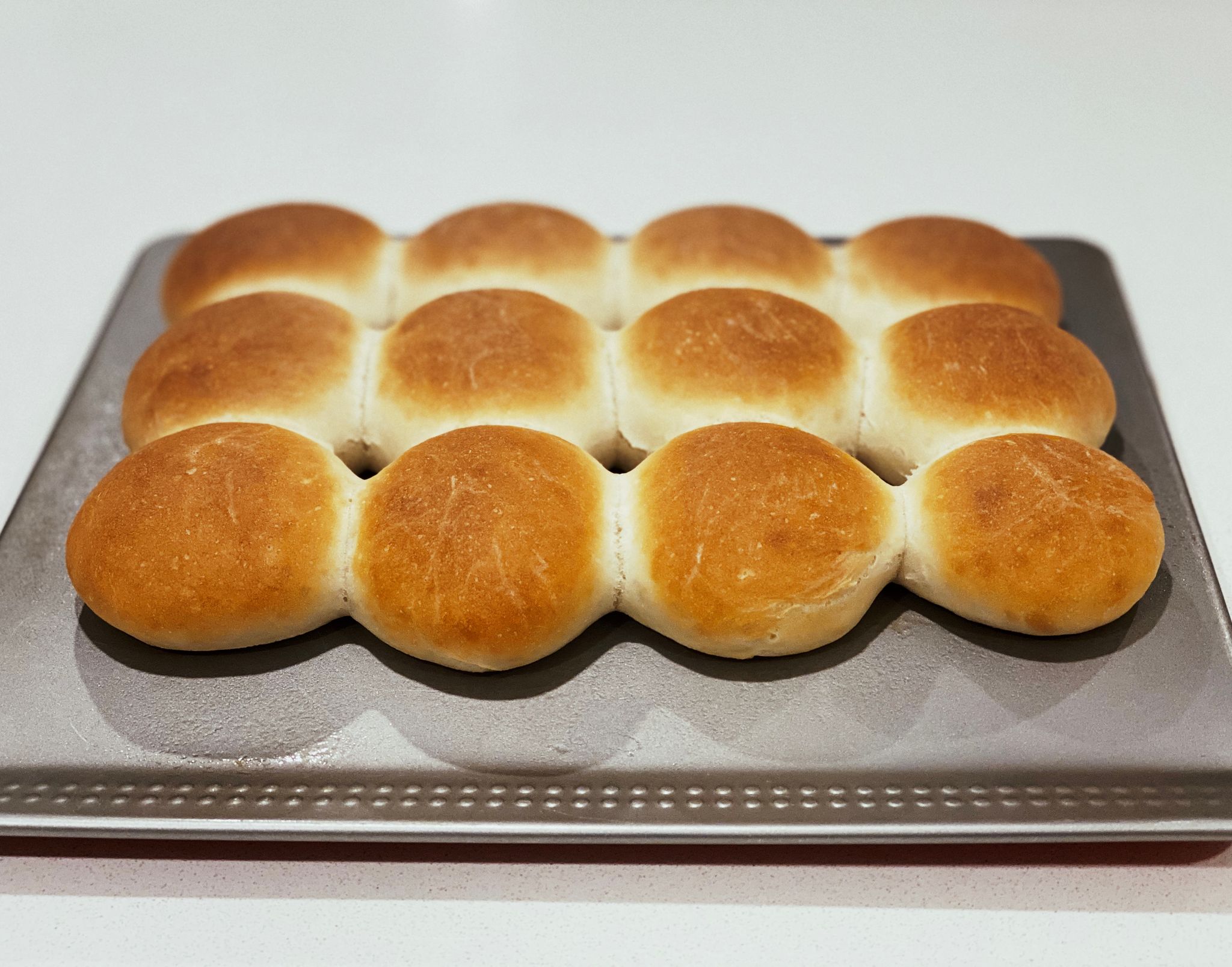 A photo of a batch of small rolls all connected to each other, sitting on an oven tray.