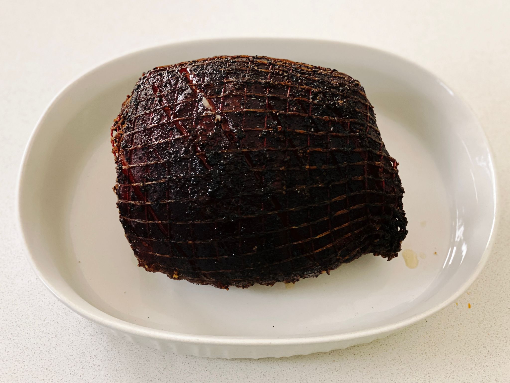 A photo of a cooked pork shoulder still in its netting. The fat layer is on top and it's all dark brown and delicious-looking.