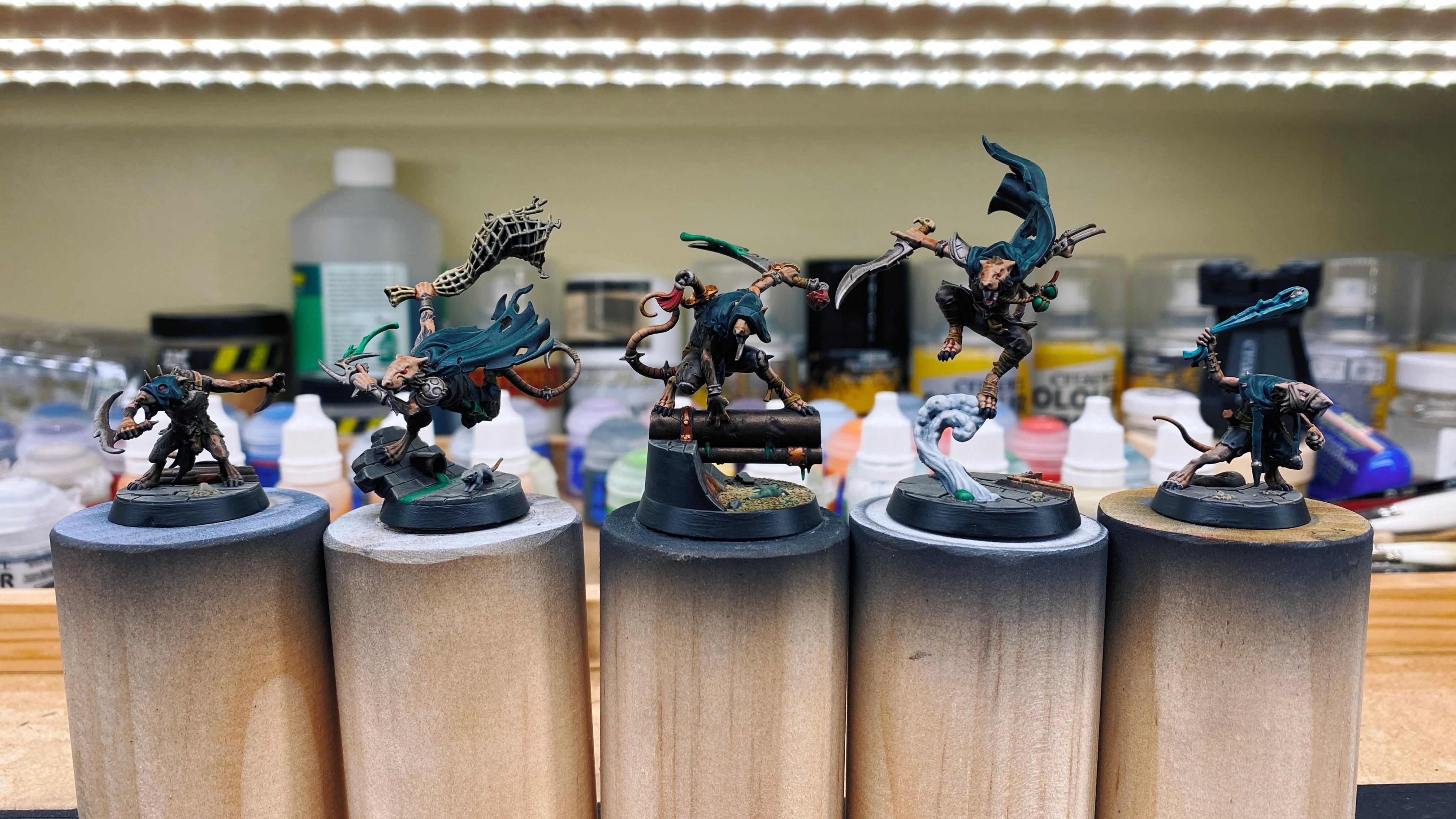 A photo of the five miniatures that make up the Skittershank's Clawpack warband. They're all rat-men with dark green cloaks and pointy weapons, and look like they're skulking about ready to assassinate someone. The bases of them make them all look like like they're in a sewer.