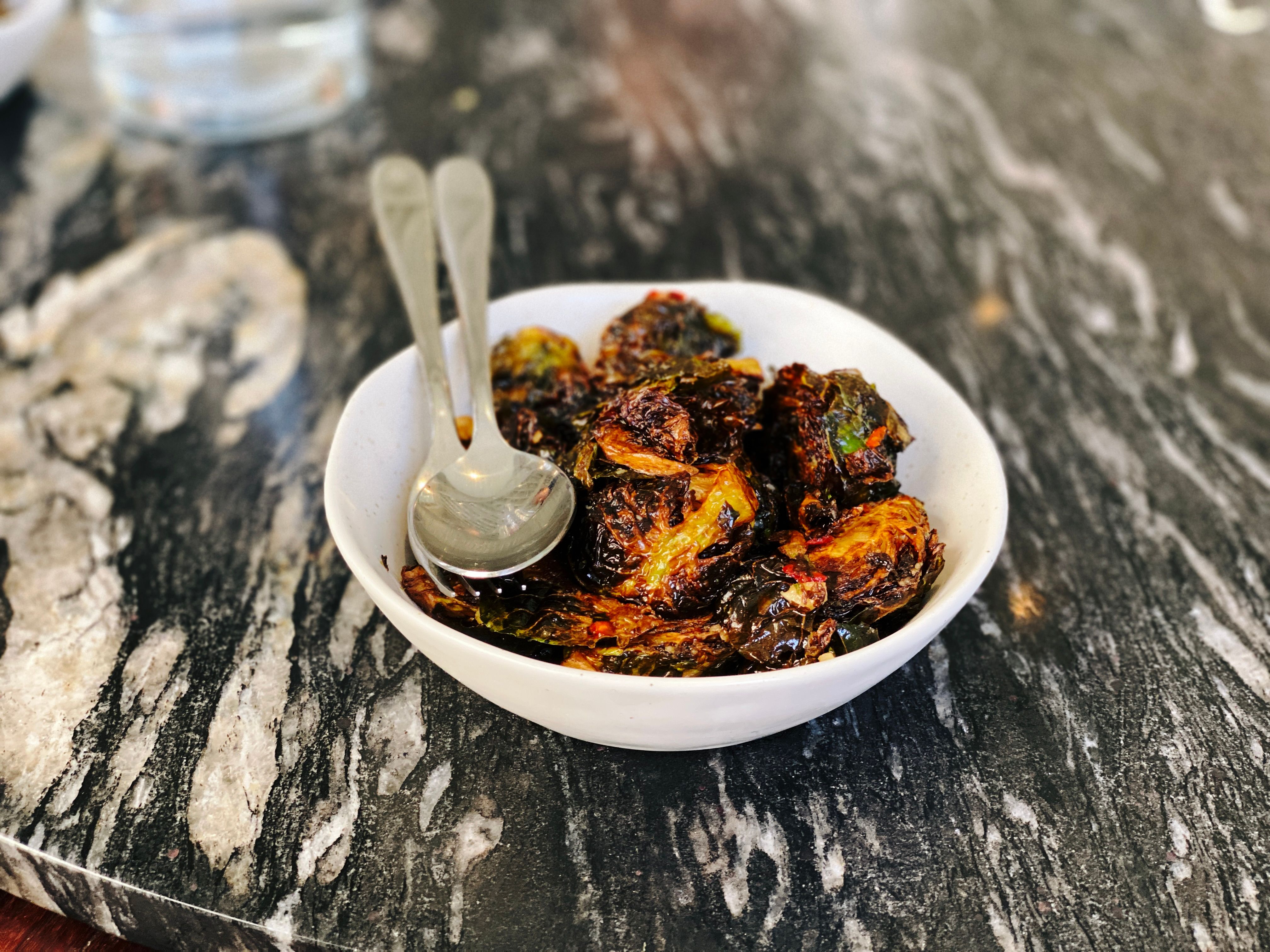 A photo of a bowl of extremely blackened hot and sour brussels sprouts with mint and red chilli.