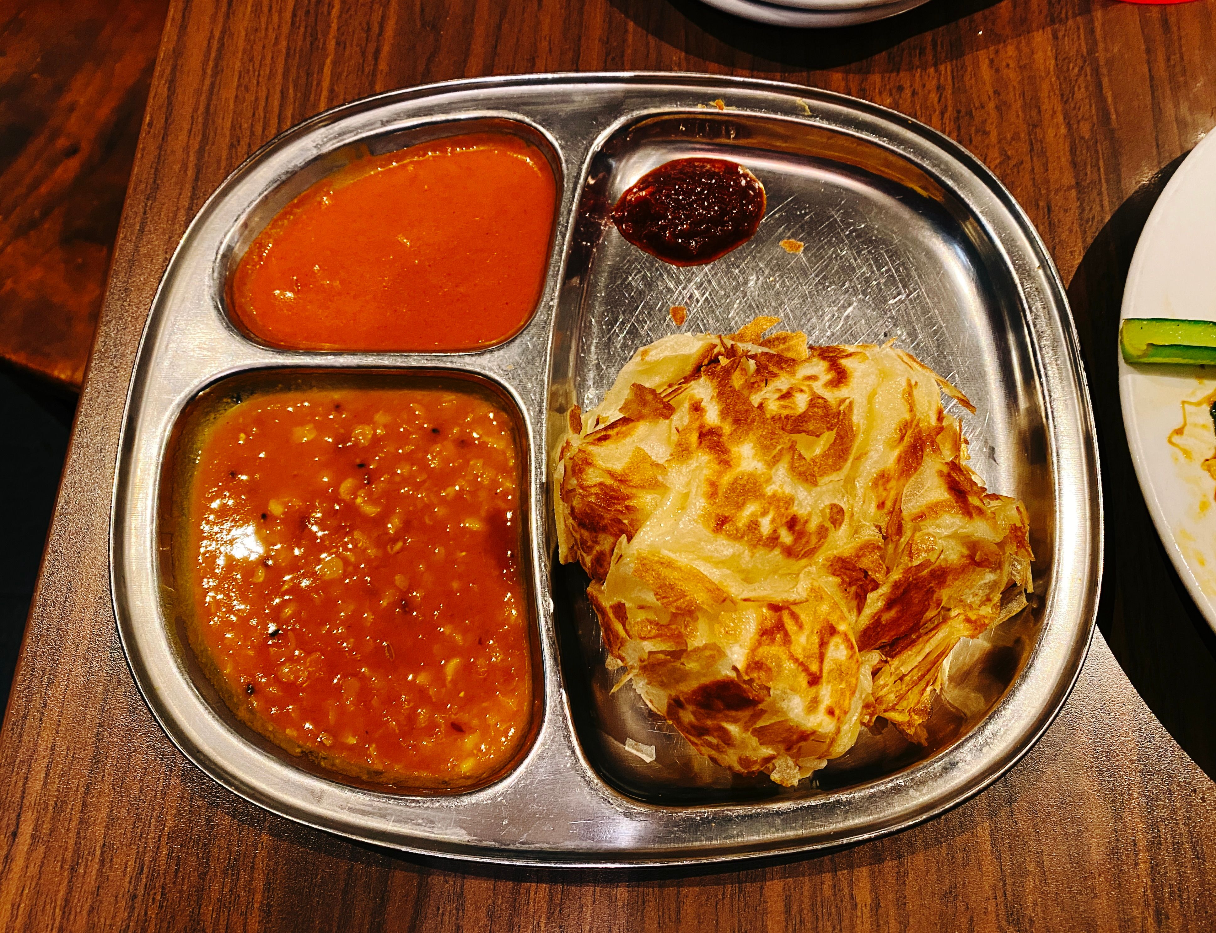 A photo of a roti canai (a flatbread thing except it's all bunched up here) on a metal plate with two different types of curry sauce to dip it into.