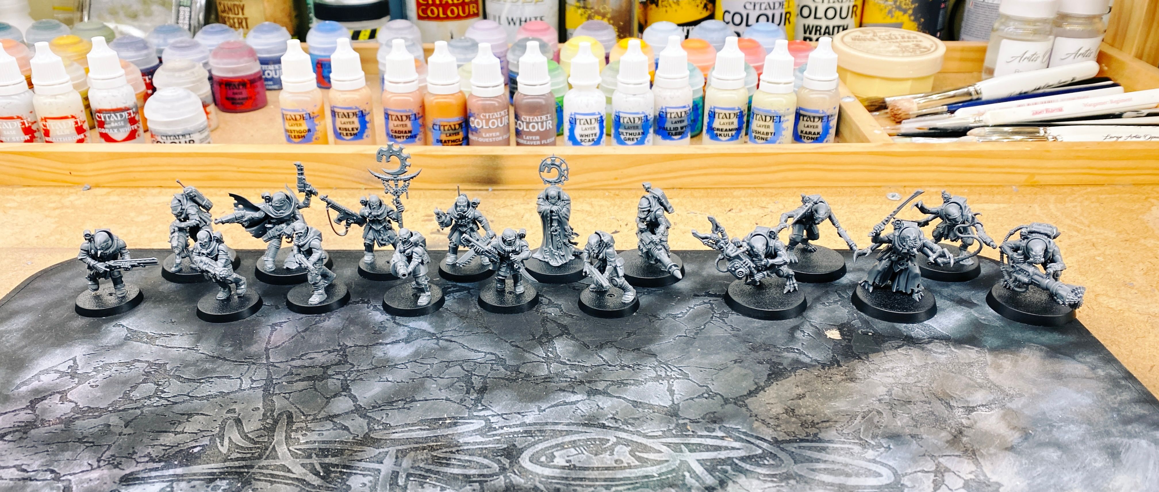 A photo of seventeen assembled miniatures in grey plastic. They're all wearing industrial-looking protective gear but their skulls are freakishly large and they're clearly not actually fully human.