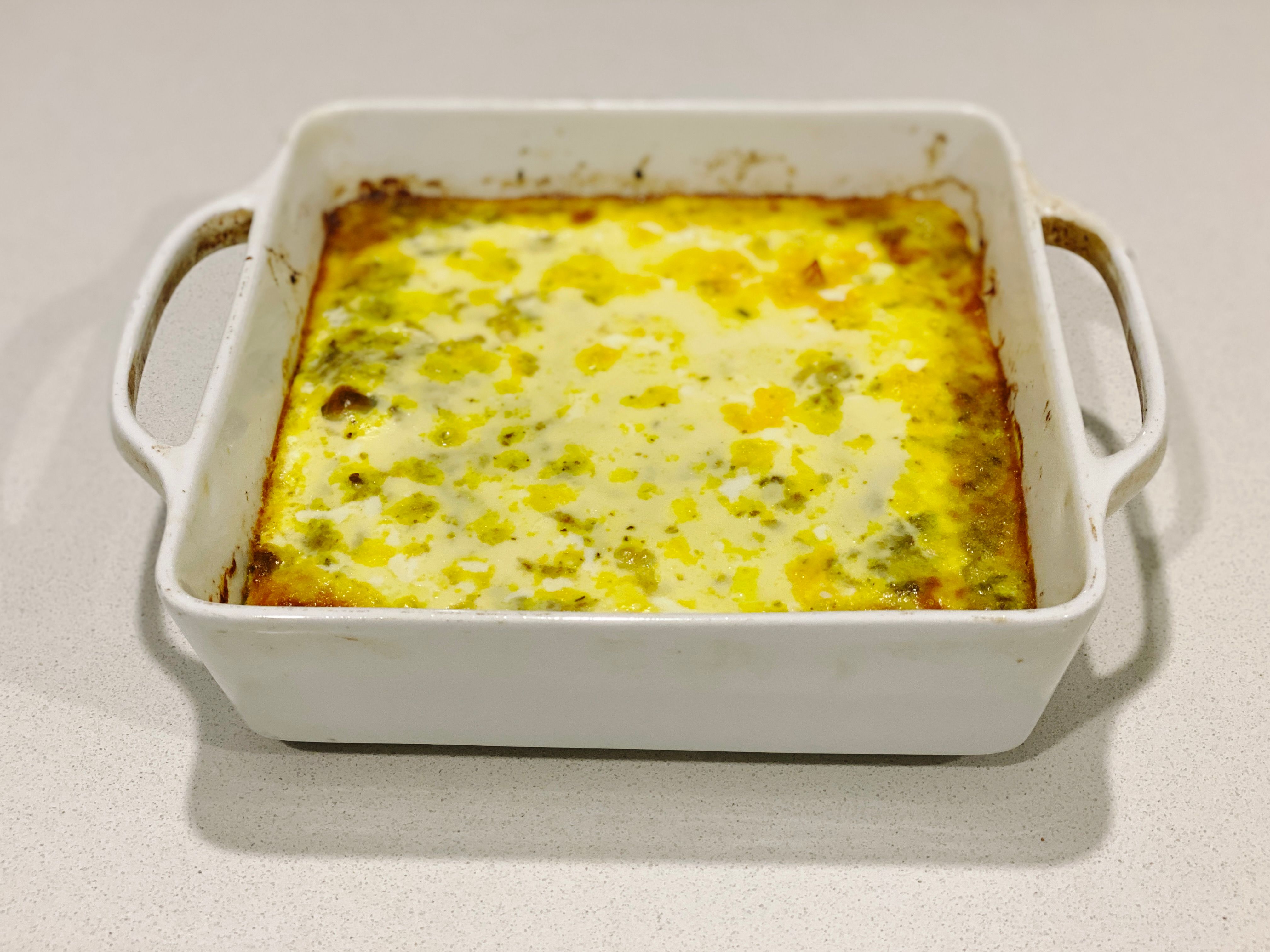 A photo of a square white baking dish with something that's been topped with egg.