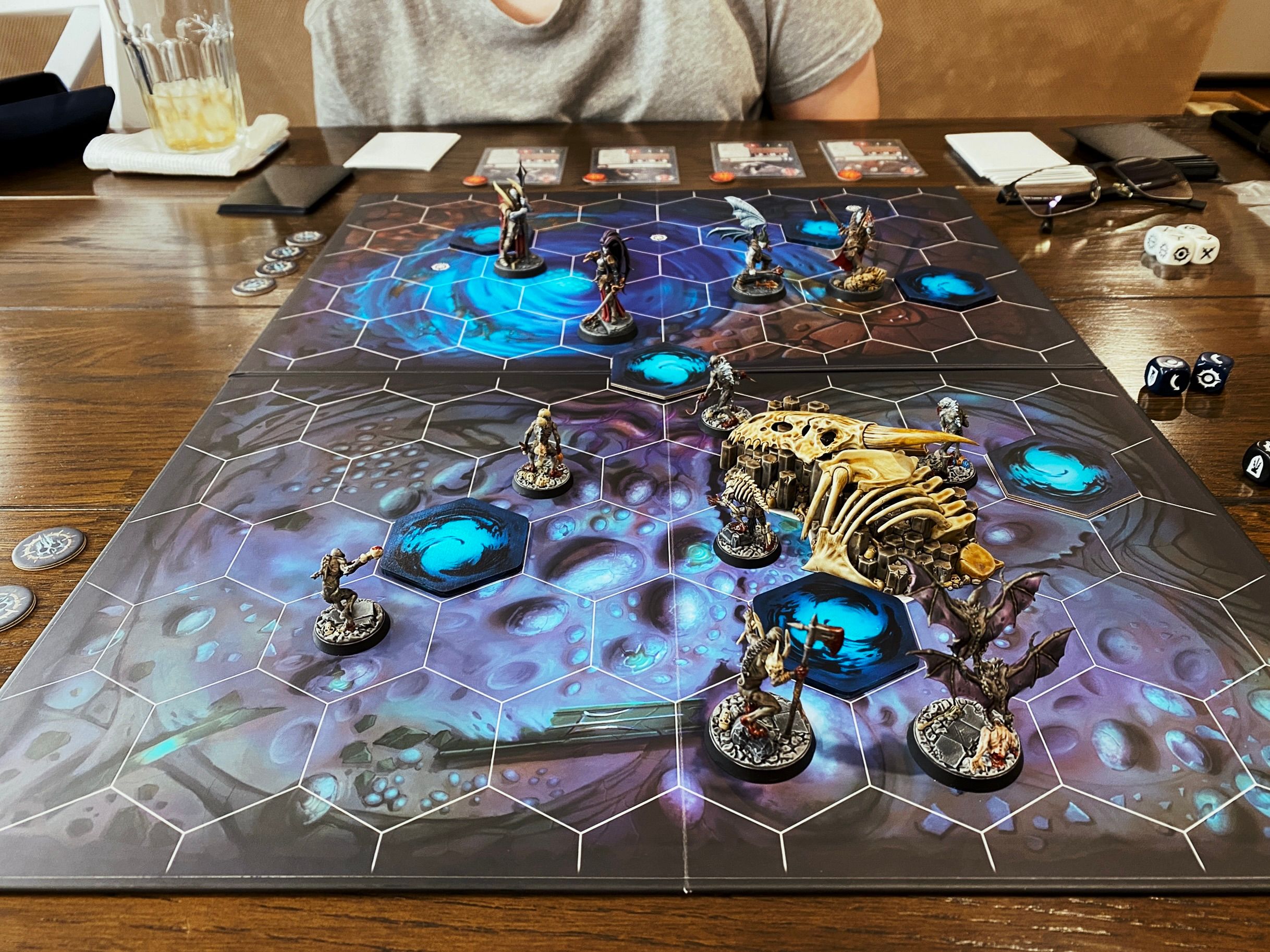 A photo of the board of Warhammer Underworlds. The board is hex-tiled and the art looks like it's in a sea cave or some underwater cavern. The two warbands are the Crimson Court (elegant vampires) and the Grymwatch (flesh-eating ghouls).