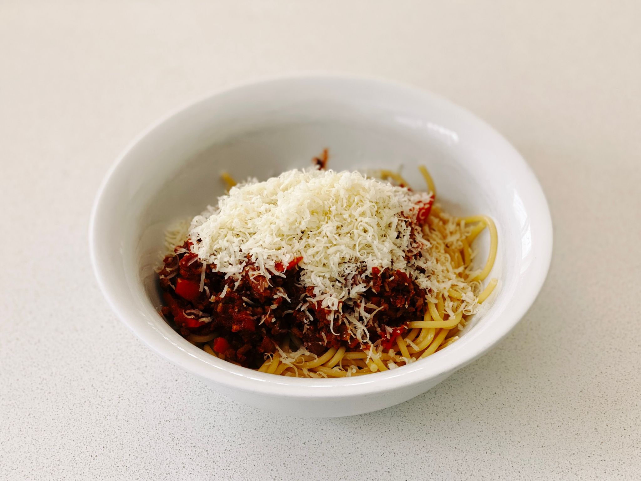 A photo of a bowl of beef bolognese sauce topped with Parmesan cheese sitting on top of spaghetti.