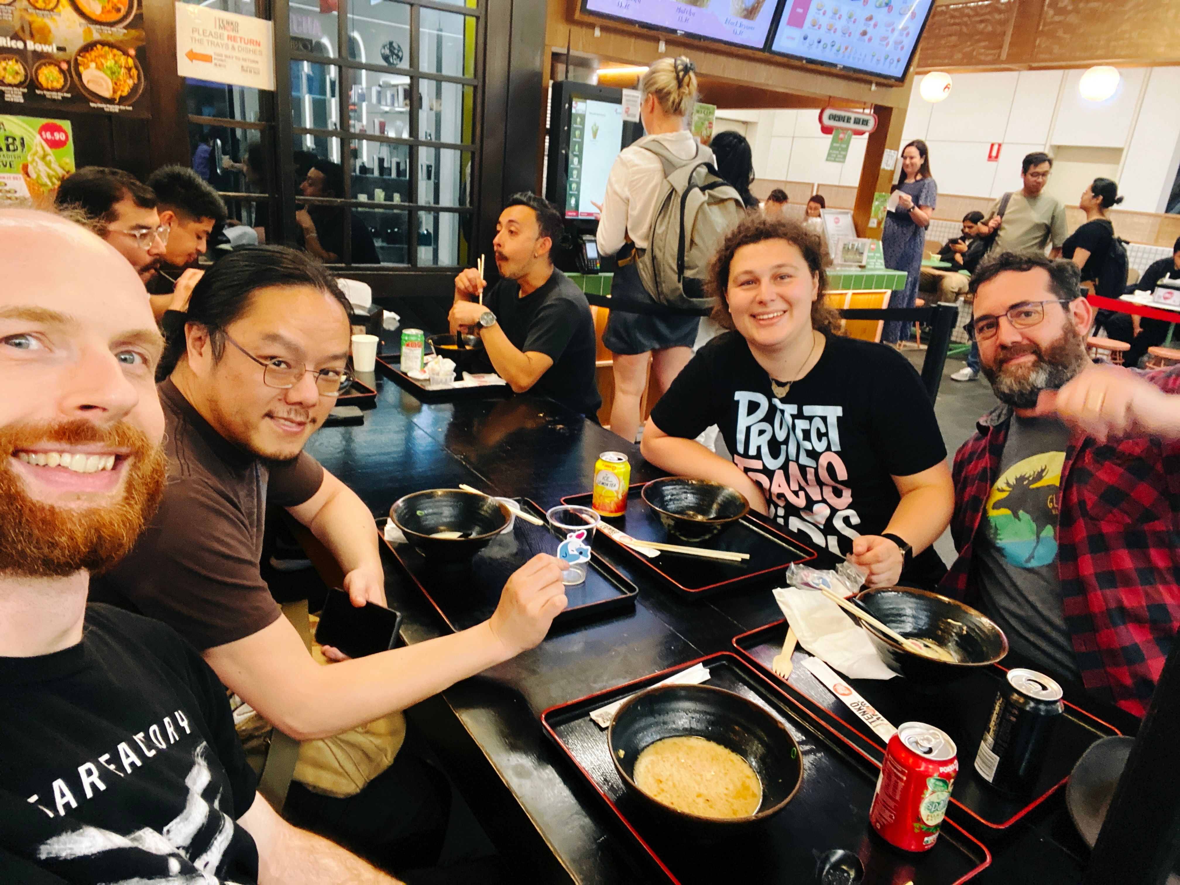 A photo of four people looking at the camera and smiling. They're sitting around a table with empty ramen bowls in it.