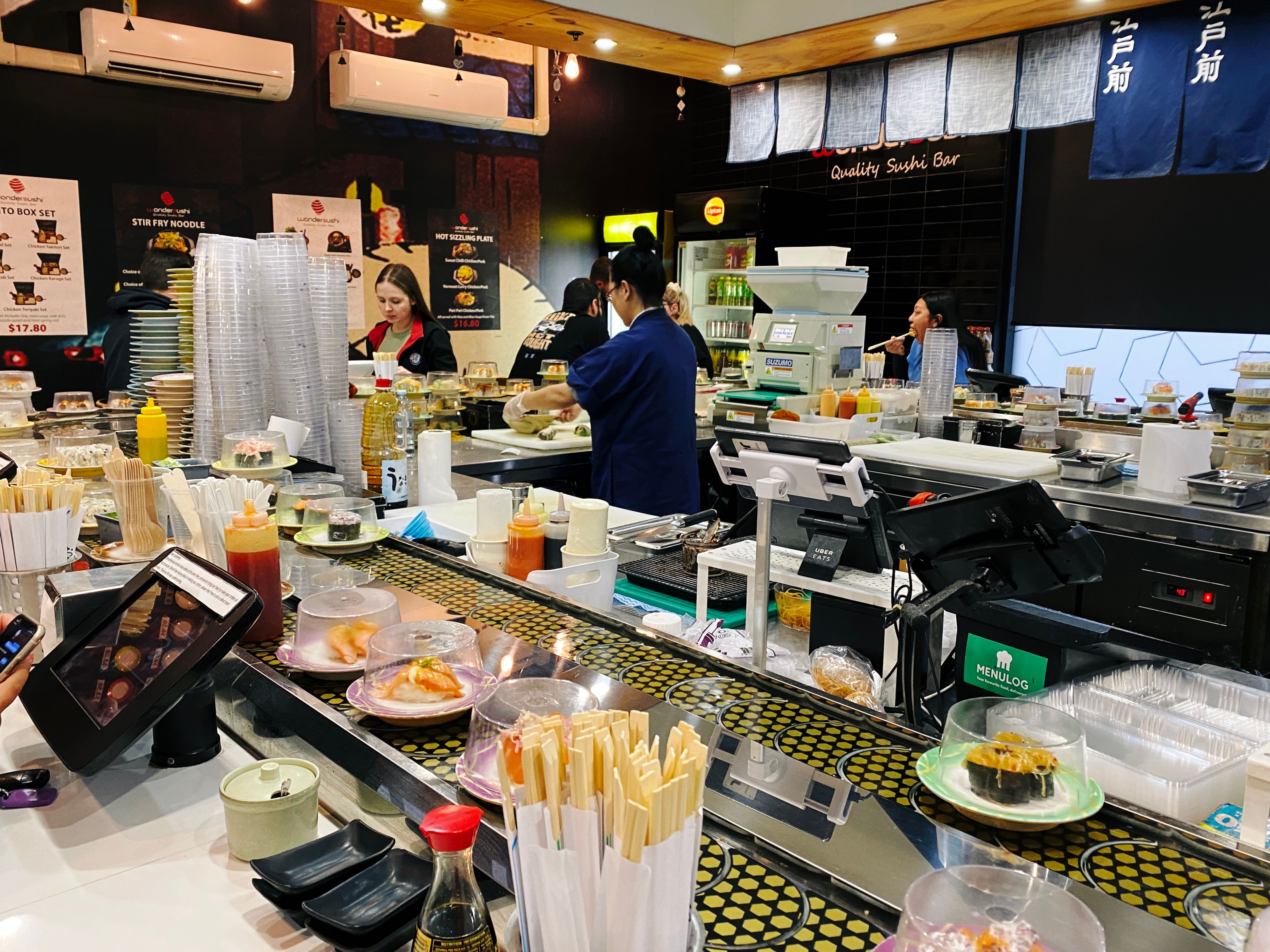 A photo of the inside of a sushi train restaurant with people in the middle making sushi.