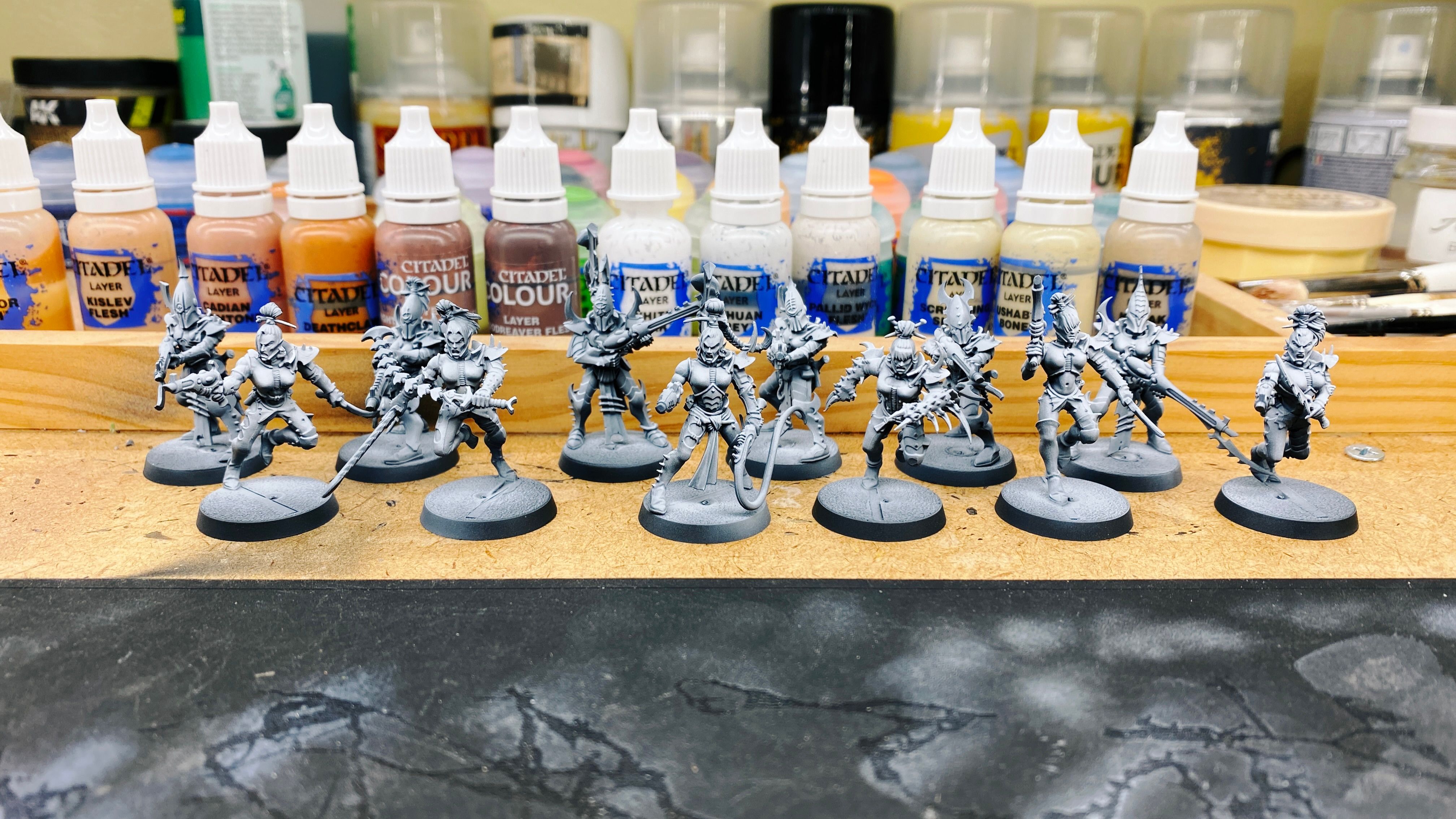 A photo of six assembled and undercoated miniatures. Drukhari are basically evil space elves, the ones at the back (the Kabalites) all have spiky armour and helmets and are pointing spiky-looking guns, and the ones at the front (the Wyches) are much more lightly armoured (but still spiky) and have knives and pistols.
