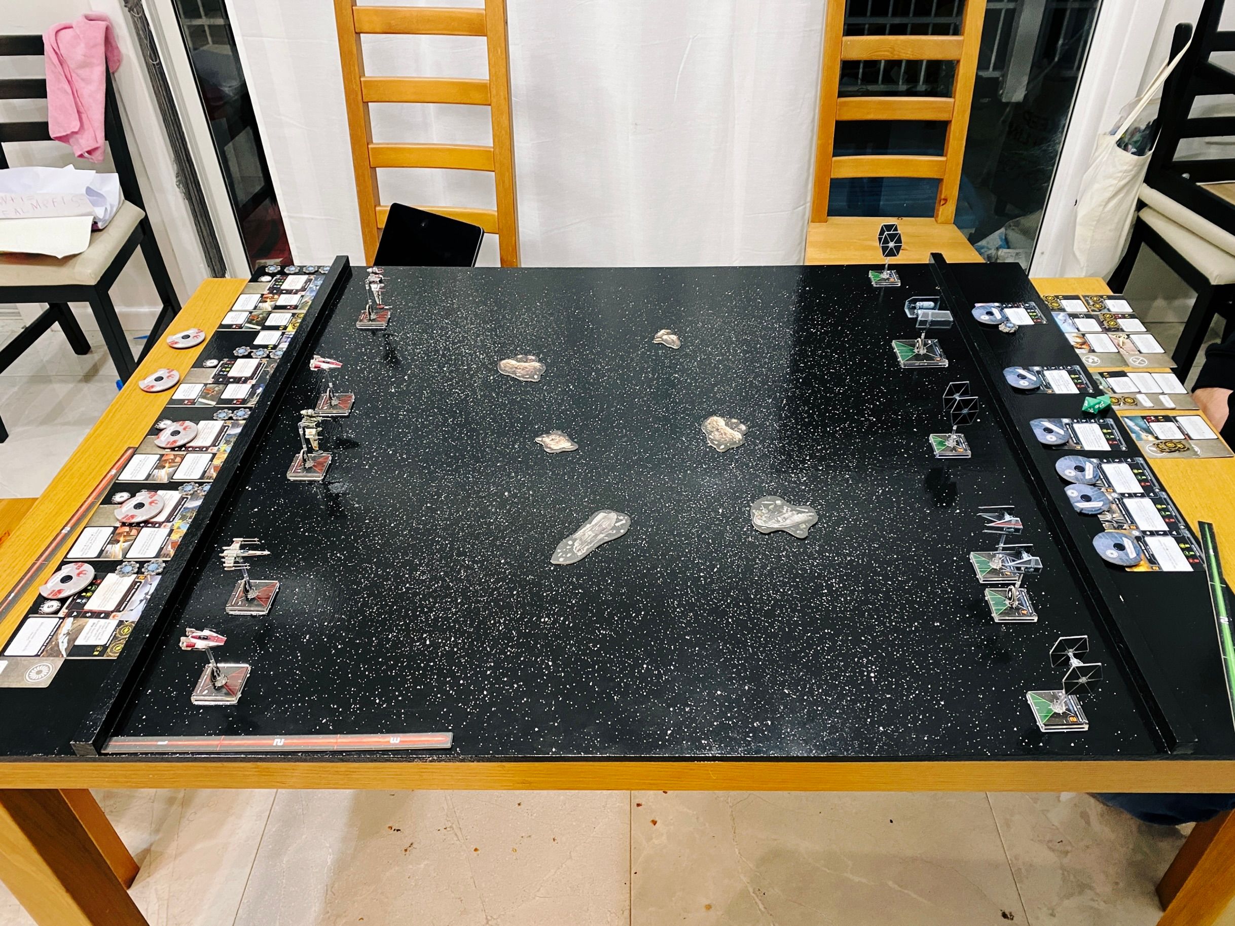 A photo of a big shiny black wooden board with stars painting on it, with two B-wings, two A-wings, and an X-wing on one side and a TIE Punisher, two TIE Interceptors, and three TIE Fighters on the other.