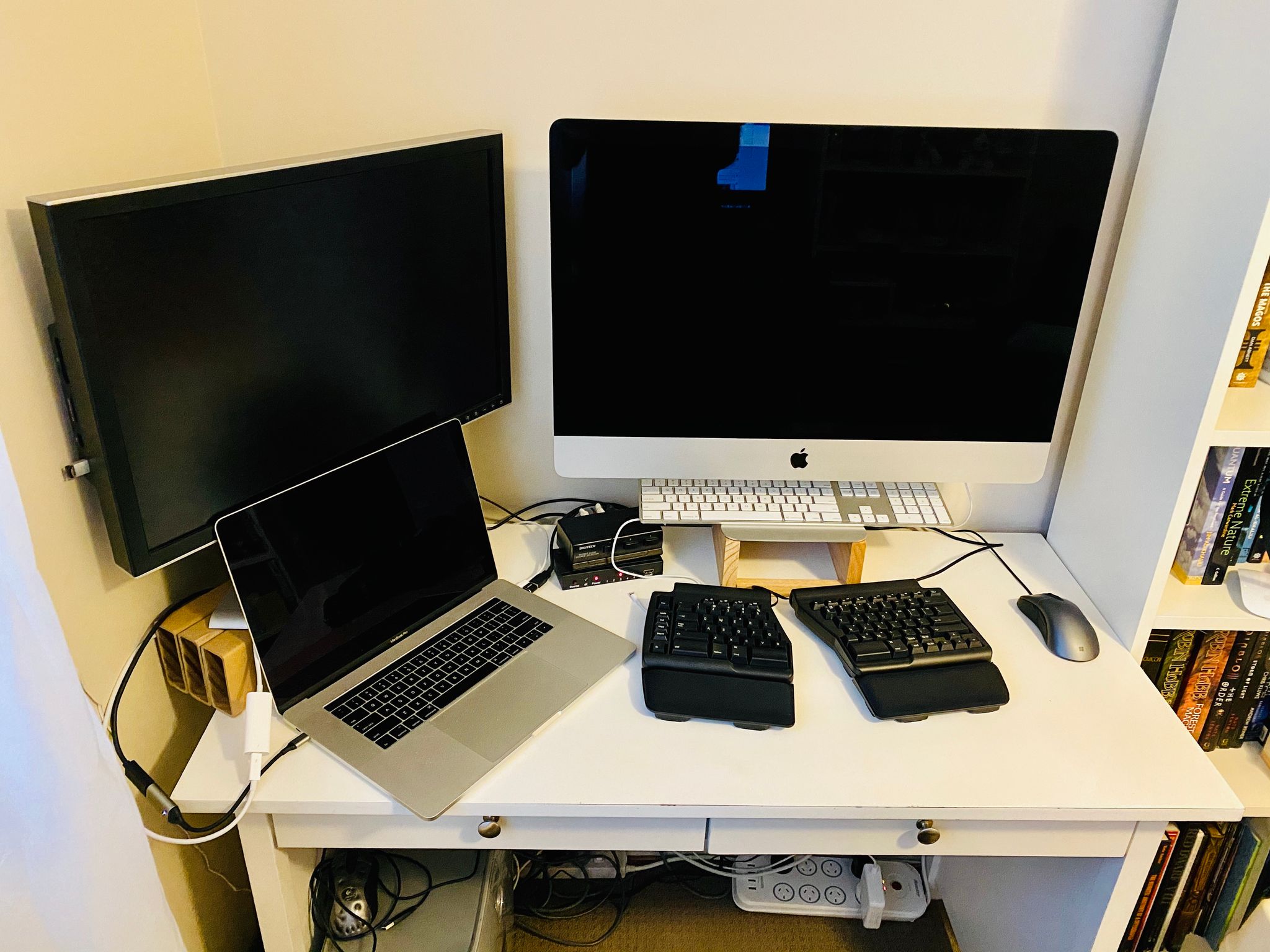 A photo of a white desk with a 27 iMac in the middle, a 24” Dell to the left, and a 15” MacBook Pro sitting in front of the Dell. There’s an ergonomic mechanical keyboard in front of the iMac.