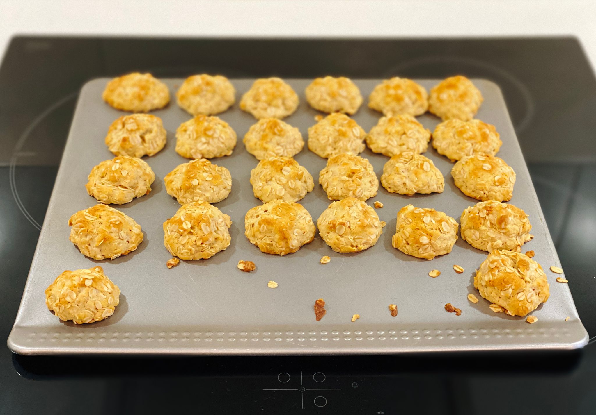A photo of a batch of small round golden brown biscuits sittting on an oven tray.