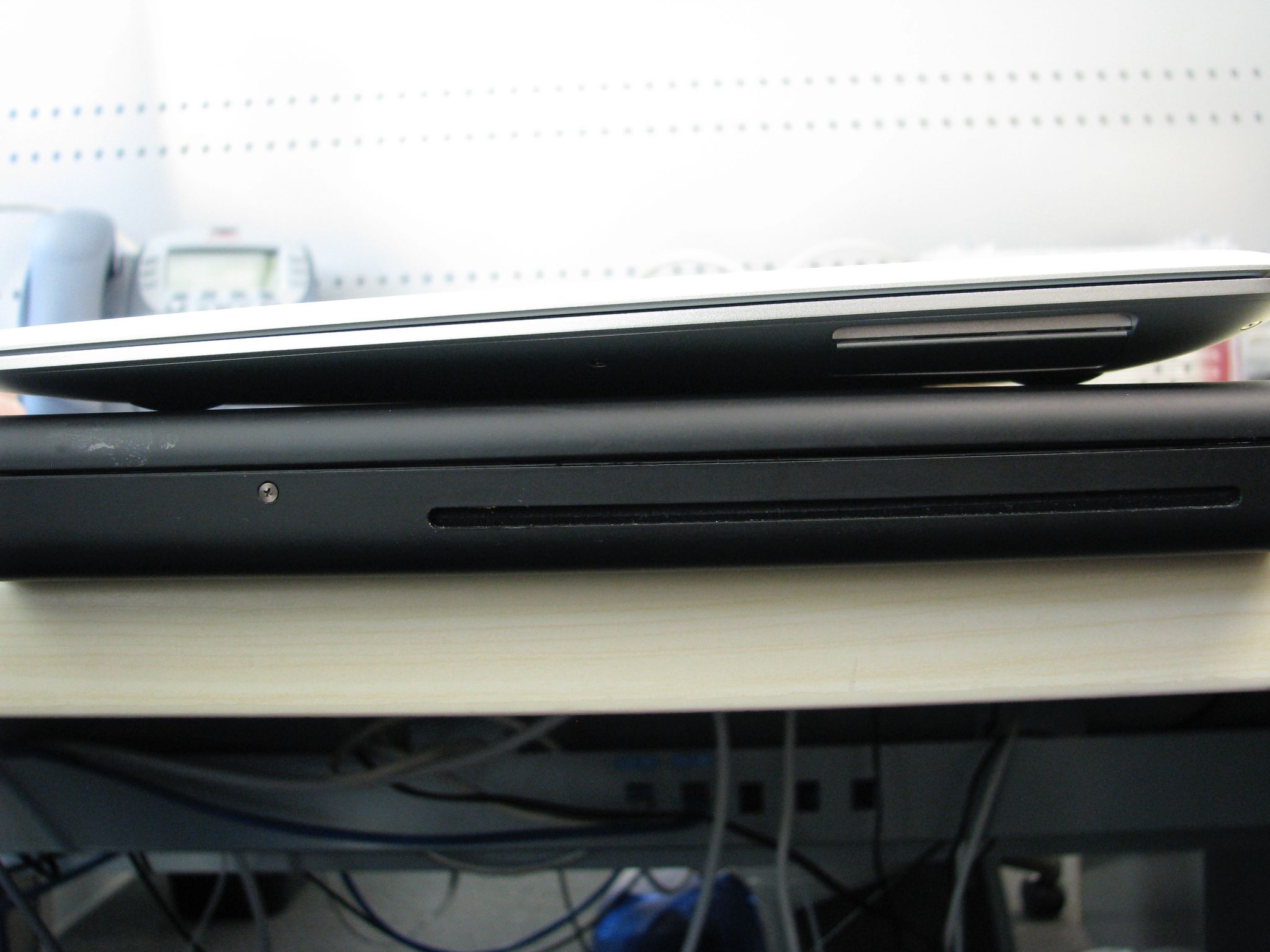 A photo taken from the side of a first-generation MacBook Air sitting on top of a black polycarbonate MacBook.