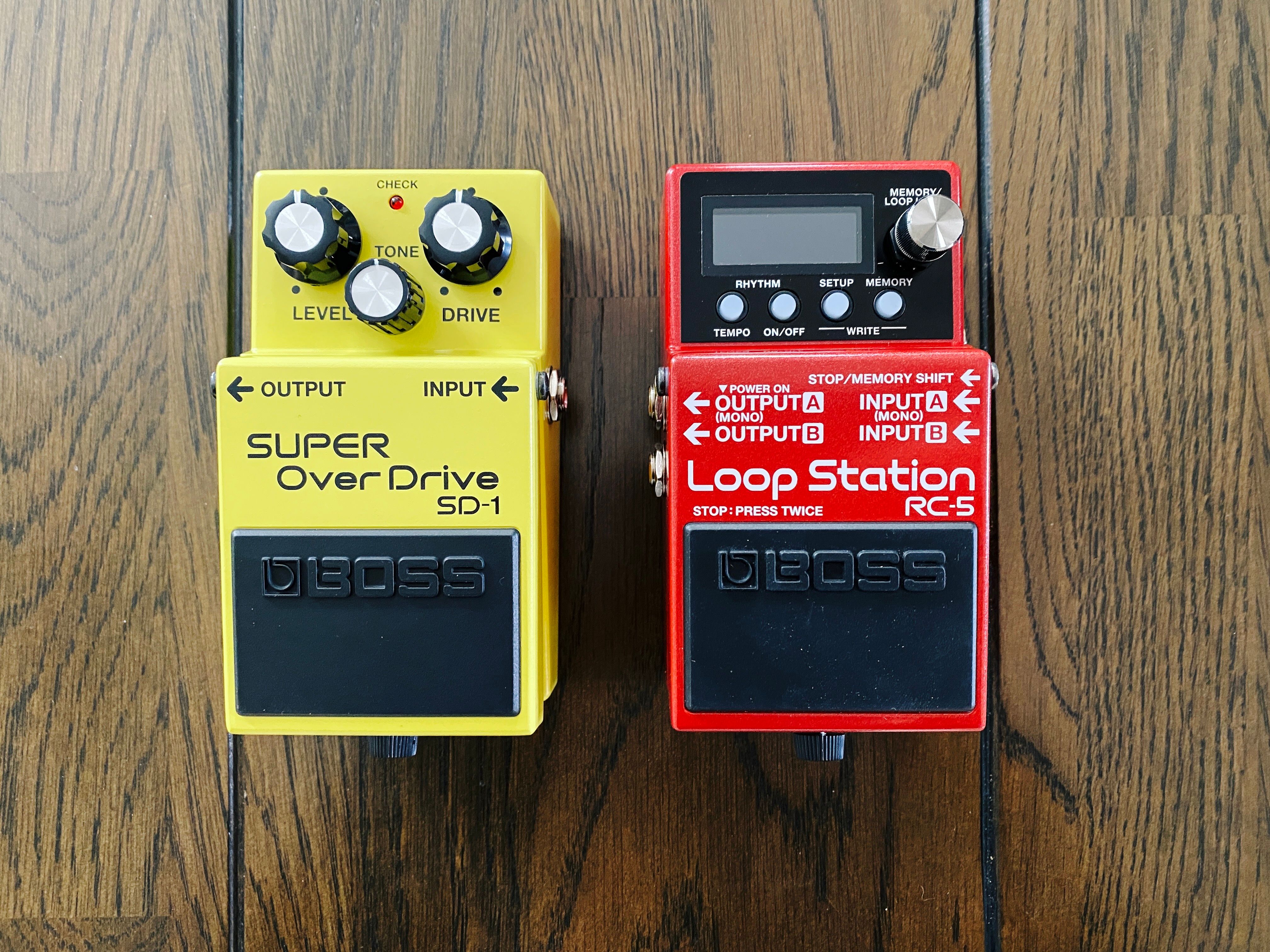 A photo of two guitar pedals, both Boss brand. One is the very yellow SD-1 "Super Overdrive" and the other is the very red RC-5 "Loop Station" looper pedal.