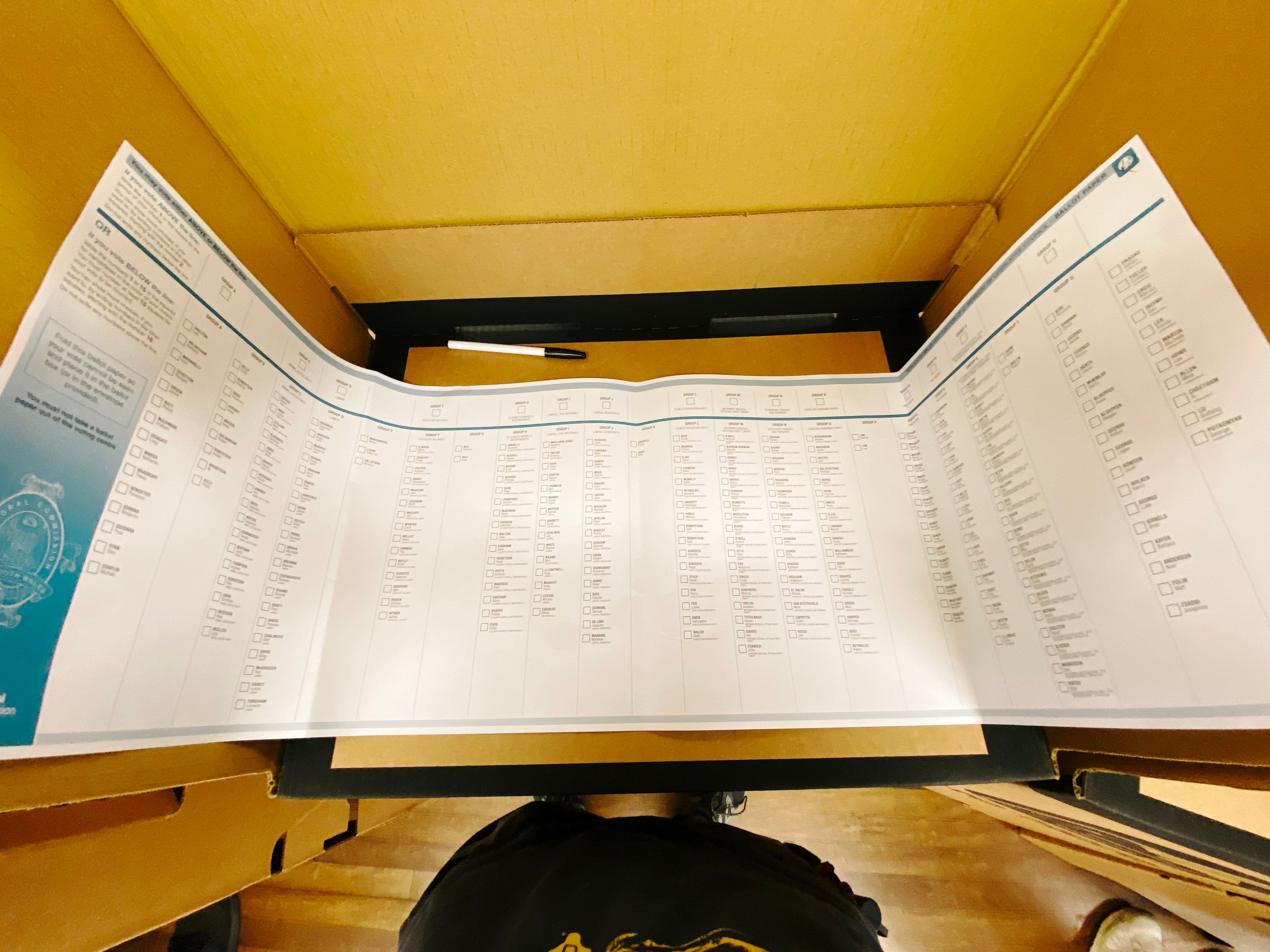 A photo of the New South Wales senate ballot paper expanded to its full width, with a ton of boxes to tick on it. It's in a cardboard voting booth and is large enough that the sides of the paper go up the sides of the booth (the booth is maybe 60cm wide).