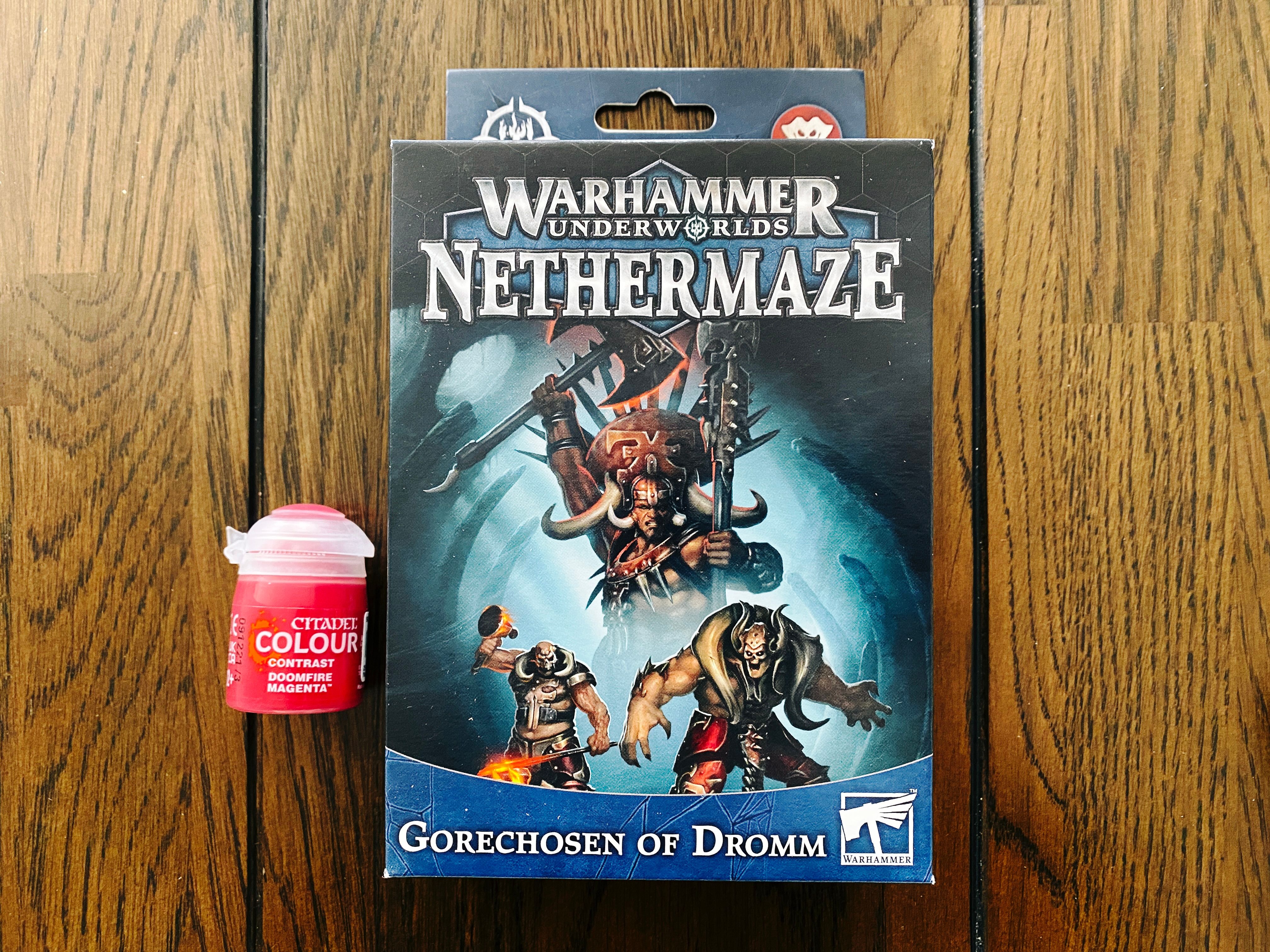 A photo of the box of the Warhammer Underworlds warband "Gorechosen of Dromm". The art on the front is three beefcake dudes, one's got a big ceremonial headdress on and is wielding an axe and a staff, one has very Immortan Joe from Max Mad vibes, and the other is part demon with absurdly large arms and big horns over his shoulders.
