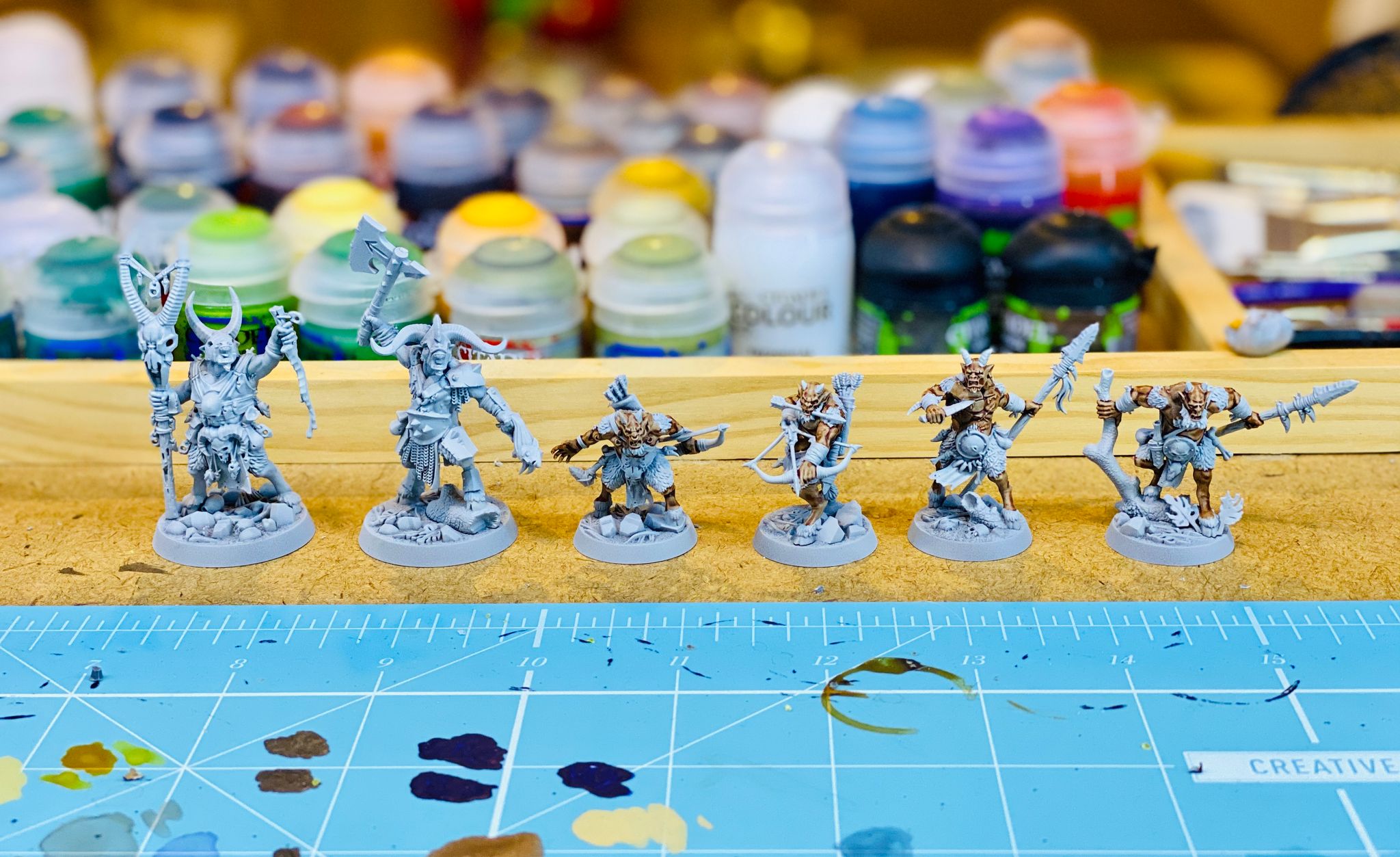 A row of six goatmen miniatures from Games Workshop's Warhammer Underworlds: Beastgrave. They're undercoated light grey, two are larger and more ferocious-looking, and the four smaller ones have their bare skin painted in a darkish flesh colour.