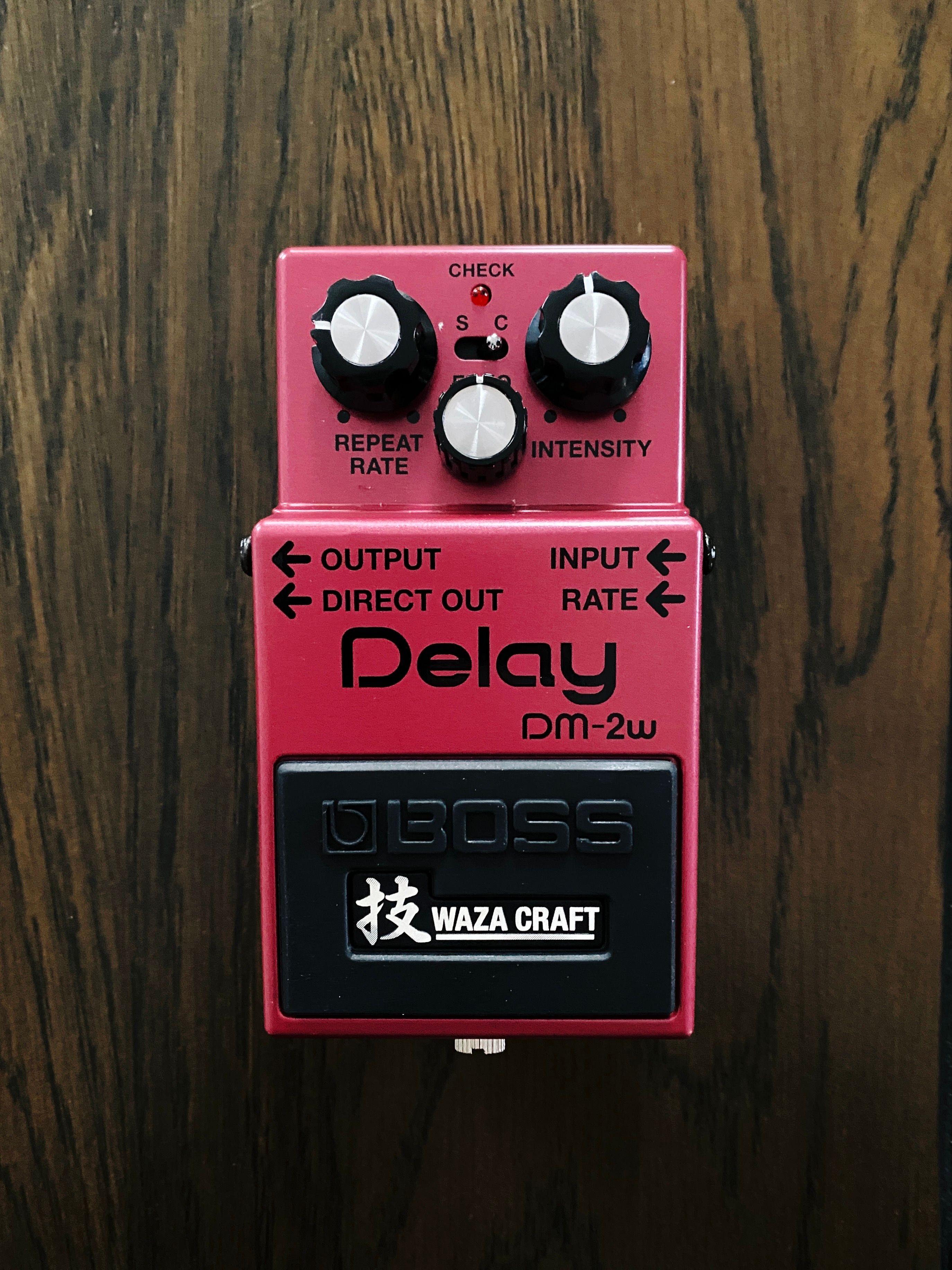 A photo of a Boss DM-2W analogue delay guitar pedal. It's a shiny sort-of-magenta colour, with three dials on the top for repeat rate, intensity, and echo.