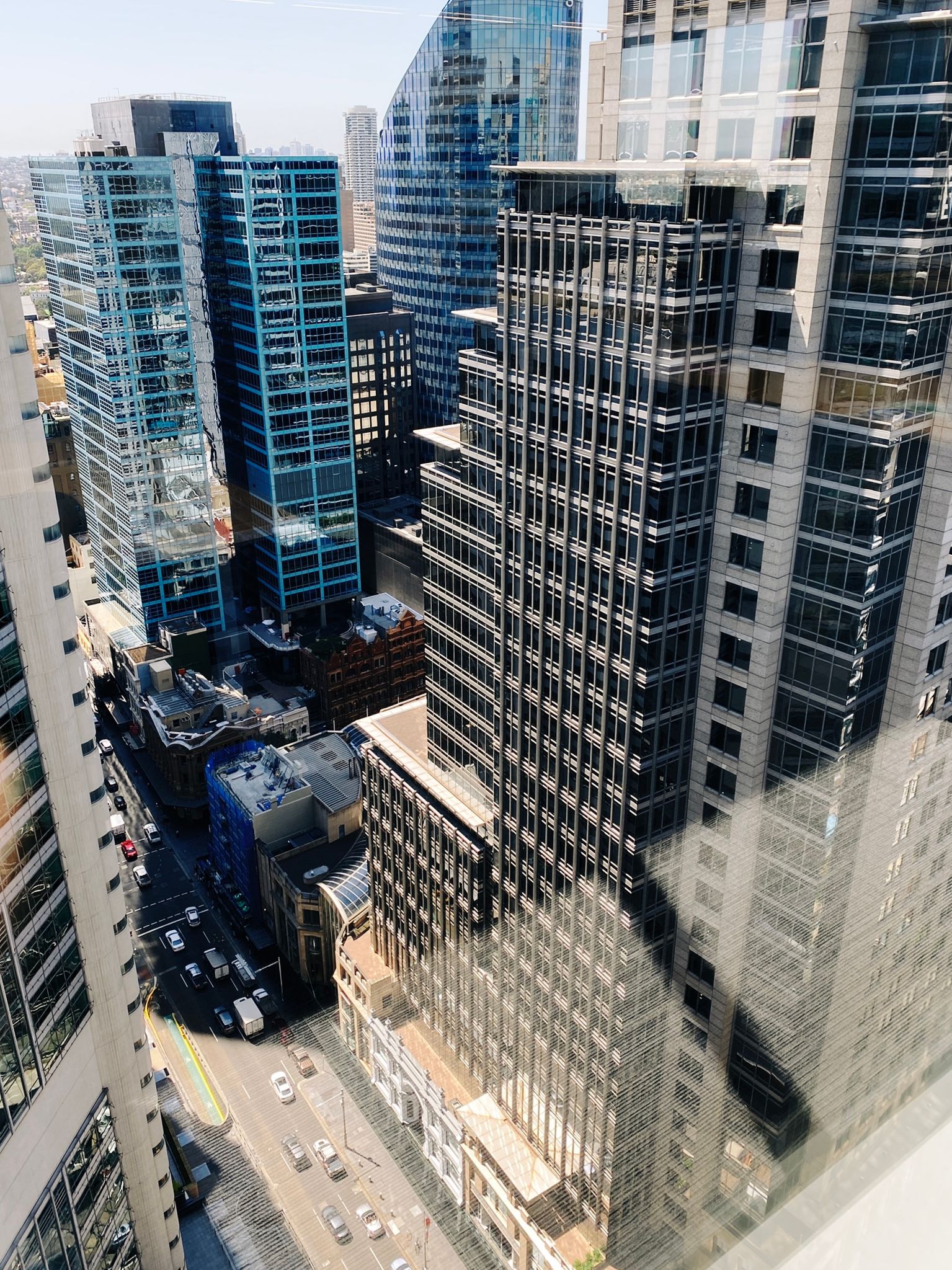 A photo looking out and down at a busy city street with tall buildings everywhere, taken from the 28th floor.