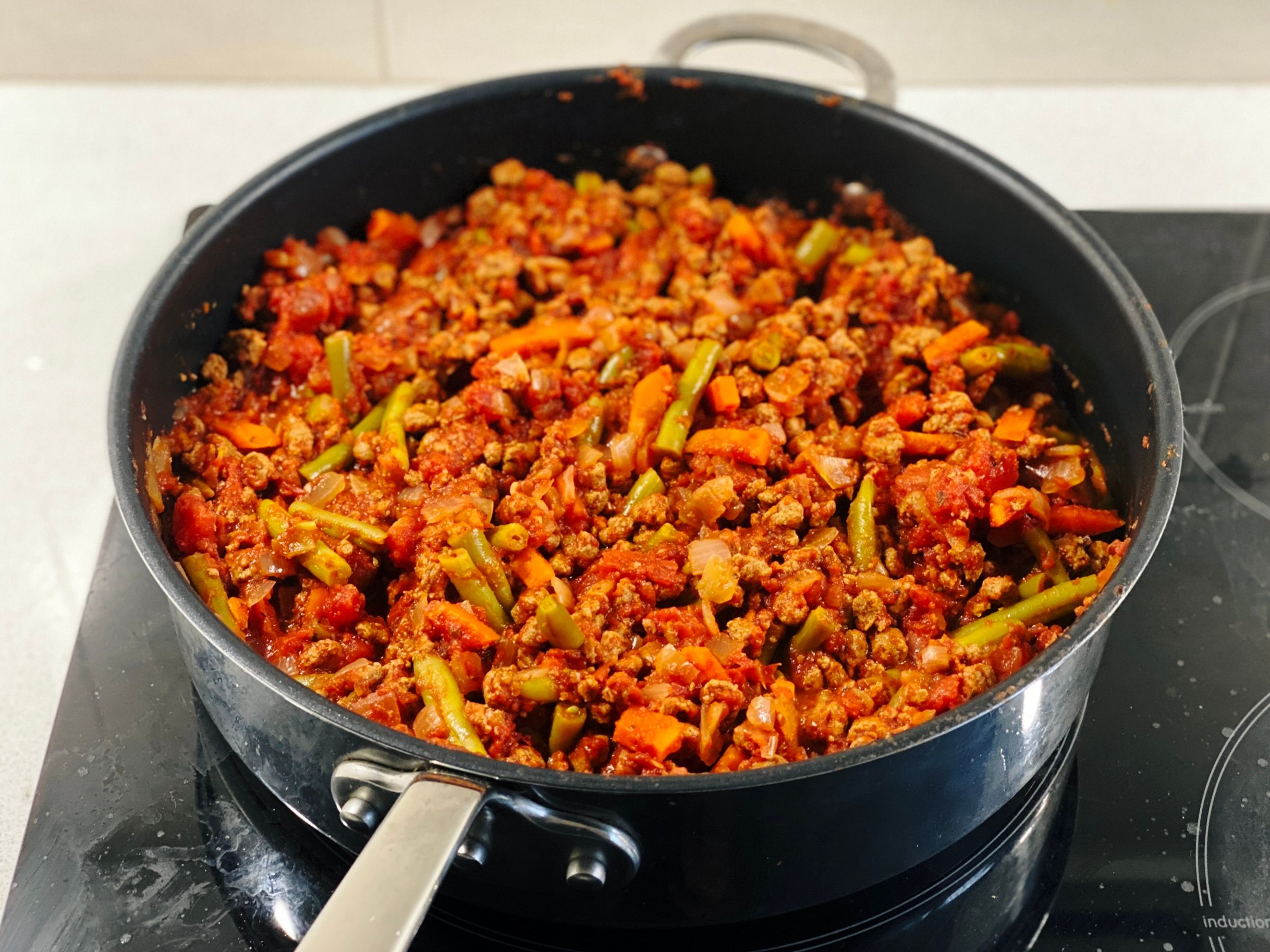 A photo of a big frying pan with absolutely chockers with what looks like bolognaise sauce with green beans and carrots in it, except it's actually not beef.