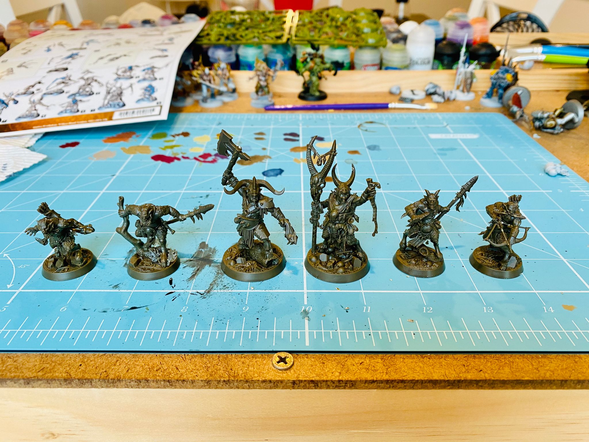 A photo of six miniatures in dark brown plastic. They're all goatmen in various poses, brandishing weapons and looking aggressive and brutish.