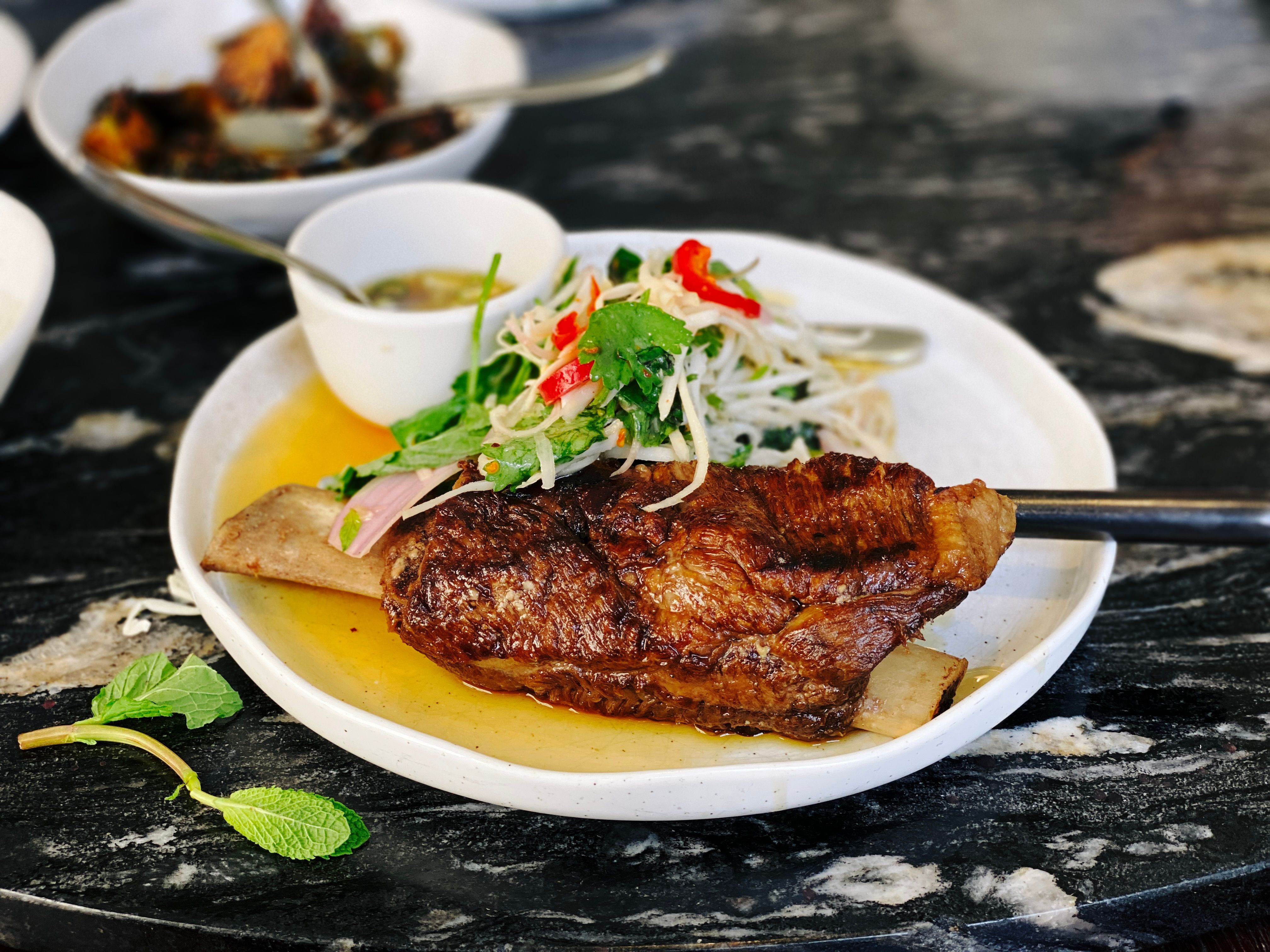 A photo of a plate with twice-cooked beef short rib with shaved coconut and prik nahm pla.