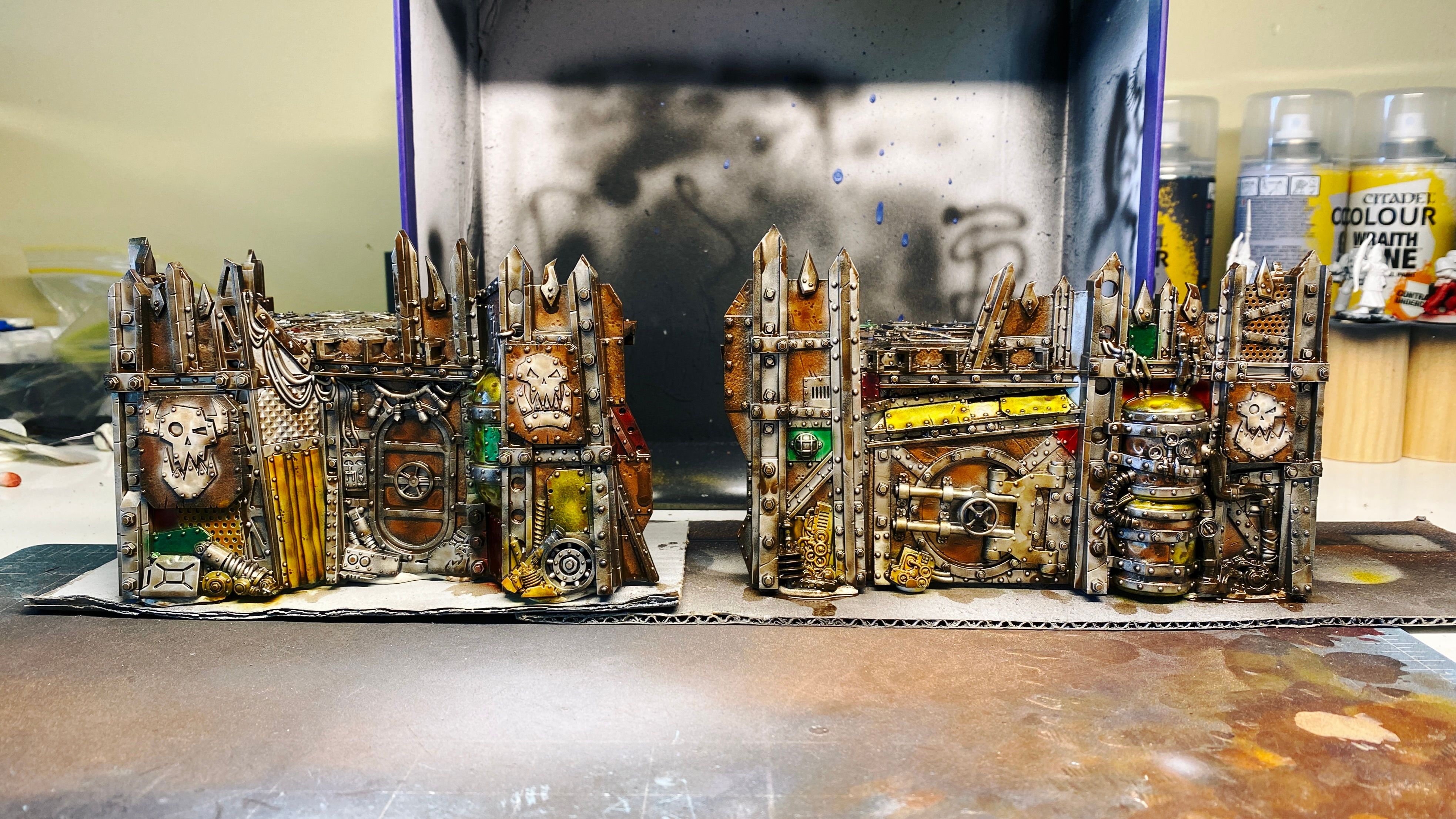 Two pieces of Warhammer 40,000: Kill Team terrain. They're parts of an Ork fort and look like they belong in a junk yard, the walls and platform on top are made up of a whole ton of pieces of metal scrap, like big plates, corrugated pieces, massive beams, there's a door in there, and a couple of empty gas cylinders. They're EXTREMELY ramshackle.