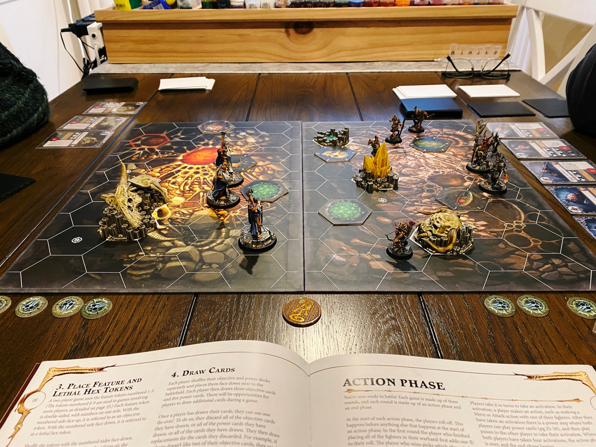 A photo of the board of a Warhammer Underworlds game. The board is has hexagonal tiles printed on it, and there's six goat-looking beastmen on the right side (Grashrak's Despoilers) and three heavily-armoured warriors in gold and dark blue armour on the left (Ironsoul's Condemnors).