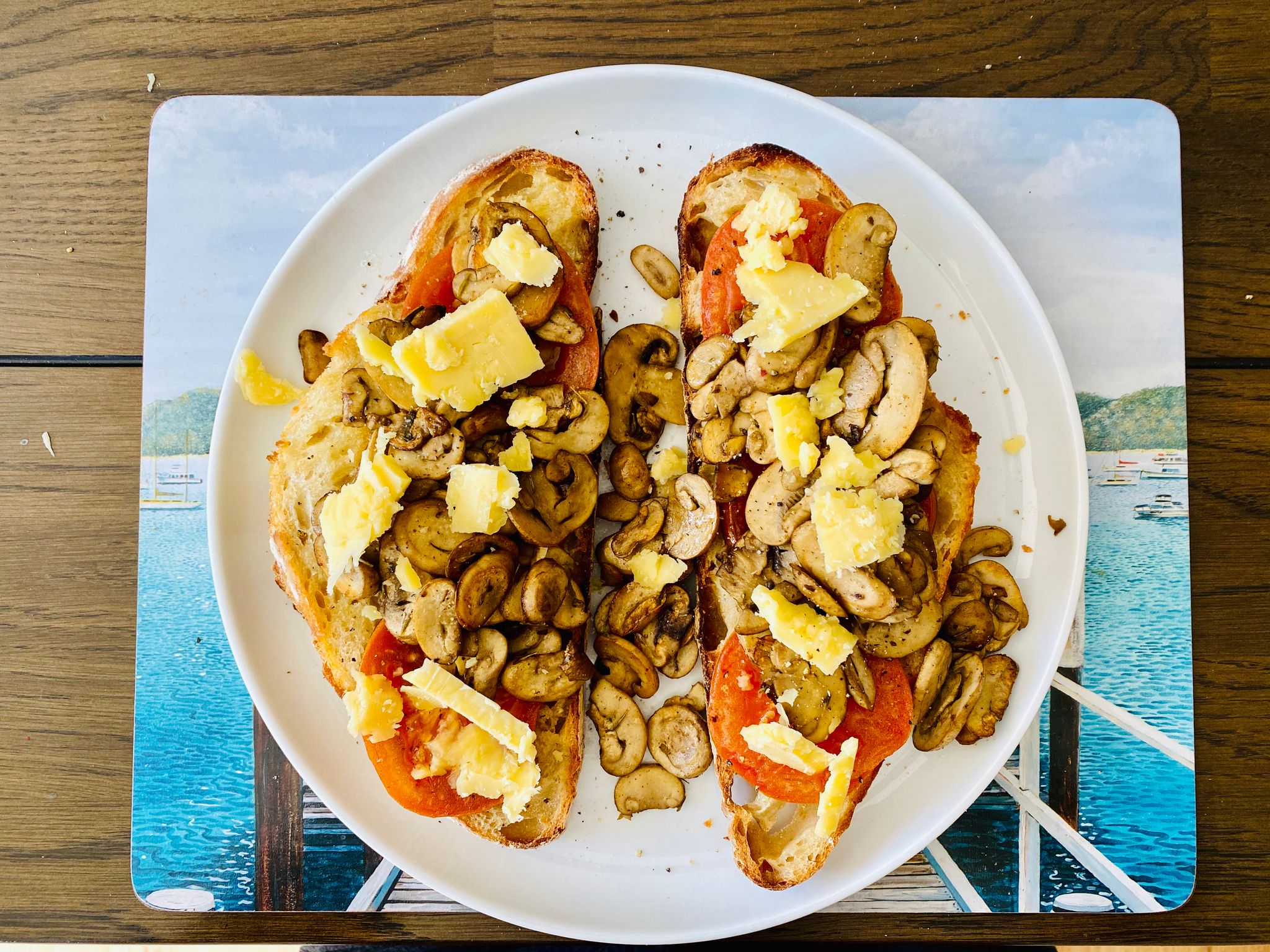 A photo of a plate with two pieces of home-made bread with grilled tomato and cooked mushrooms on top, sprinkled with chunks of fancy cheddar cheese.