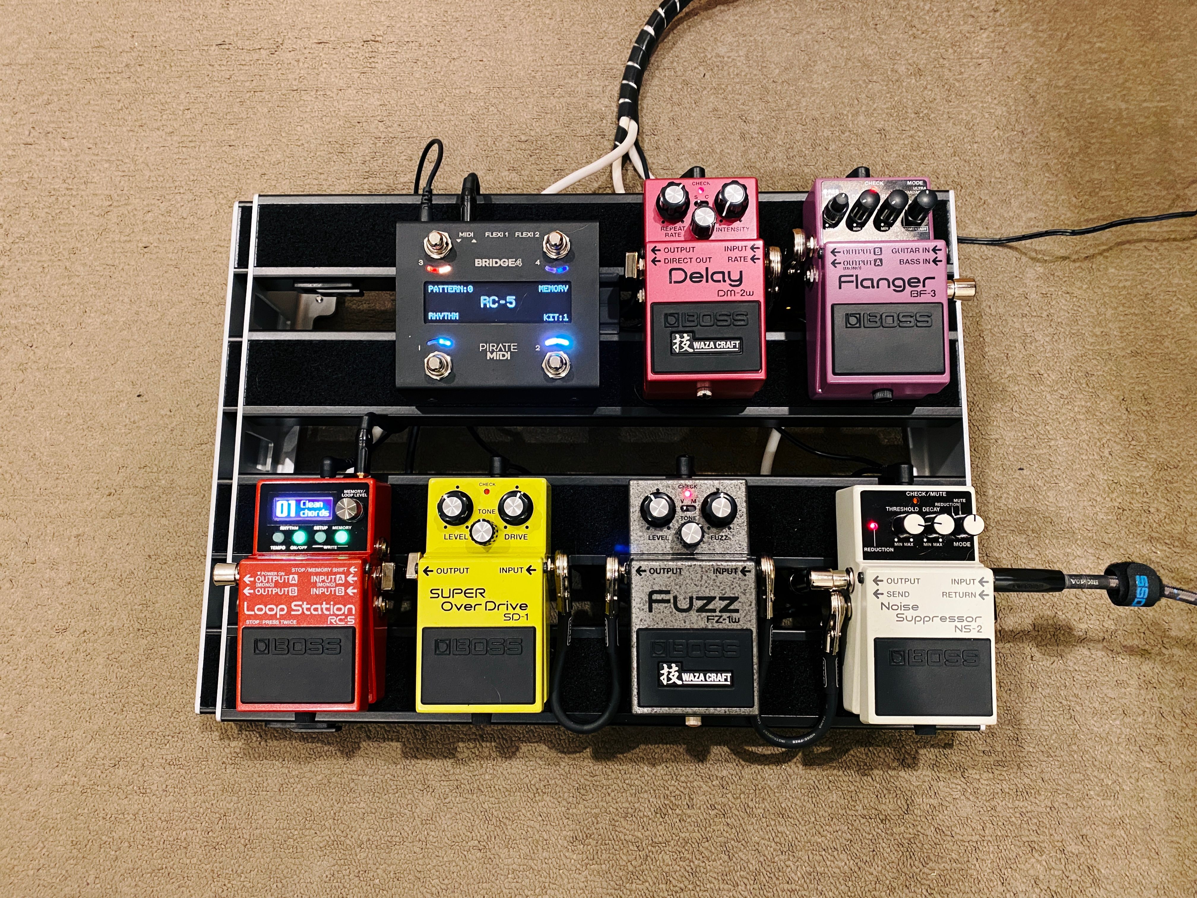 A photo of a two-row pedal board with seven pedals of various sorts on it.
