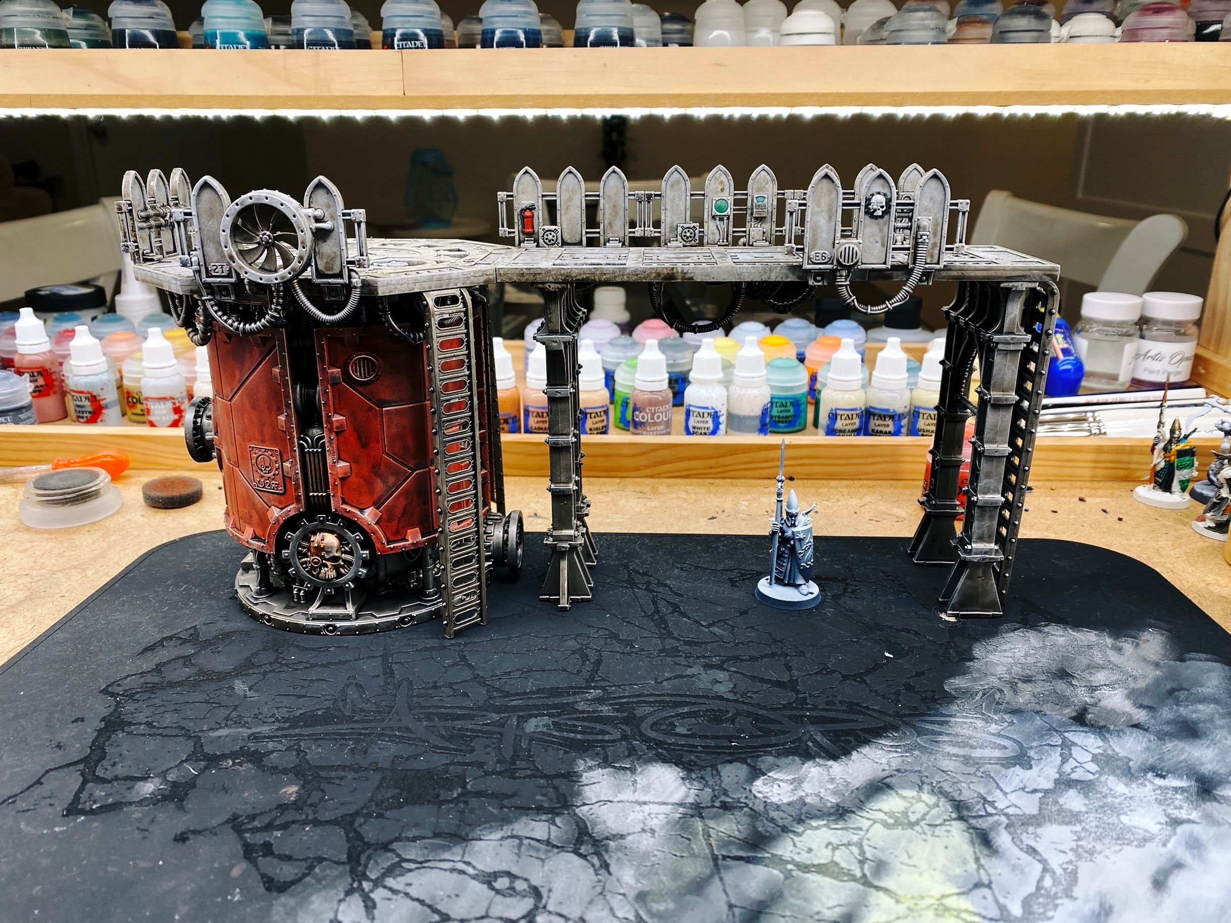 A photo of the "Ferratonic Incinerator" terrain from Warhammer 40,000. It's a massive rusty-looking cylindrical furnace with a platform on top and a gantry that extends across to the right. There's all sorts of pipes and wires and controls all over the whole thing and it's borderline steampunk but also very industrial.