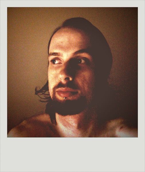 A selfie of me, a white man with a red goatee and shoulder-length hair. I'm not wearing a shirt and you can just see the top of my shoulders, and I'm looking off to the side. The photo looks like it was taken with a Polaroid camera, all the colours are very much towards the yellow and red end of the spectrum.