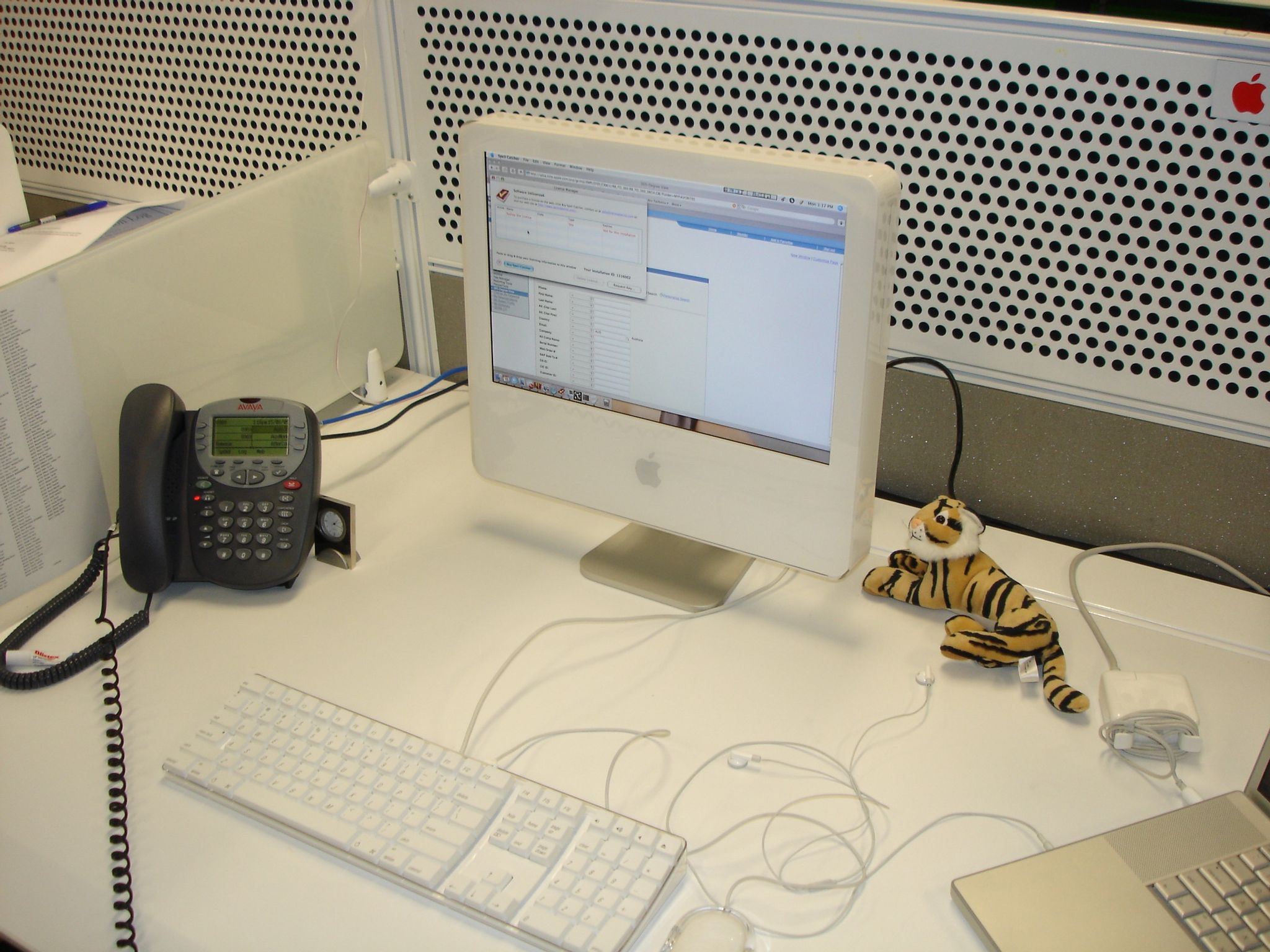 A photo of an iMac G5 sitting on a desk, with a grey call-centre phone to the left of it and a stuffed tiger toy to the right.