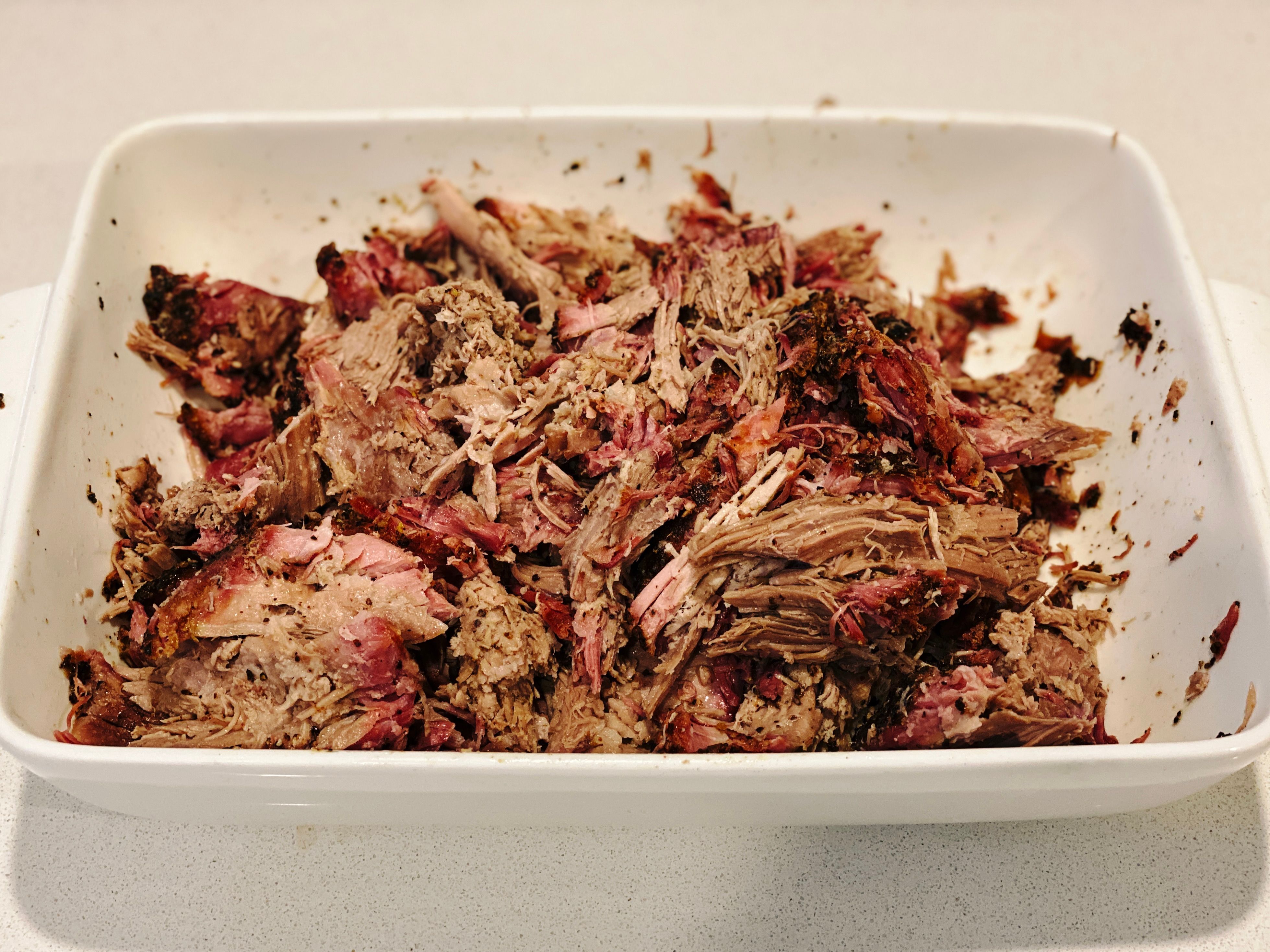 A photo of a big white dish with smoked pulled pork in it that's been all pulled apart. There's an absolutely magnificent-looking pink smoke ring in the pieces of meat.