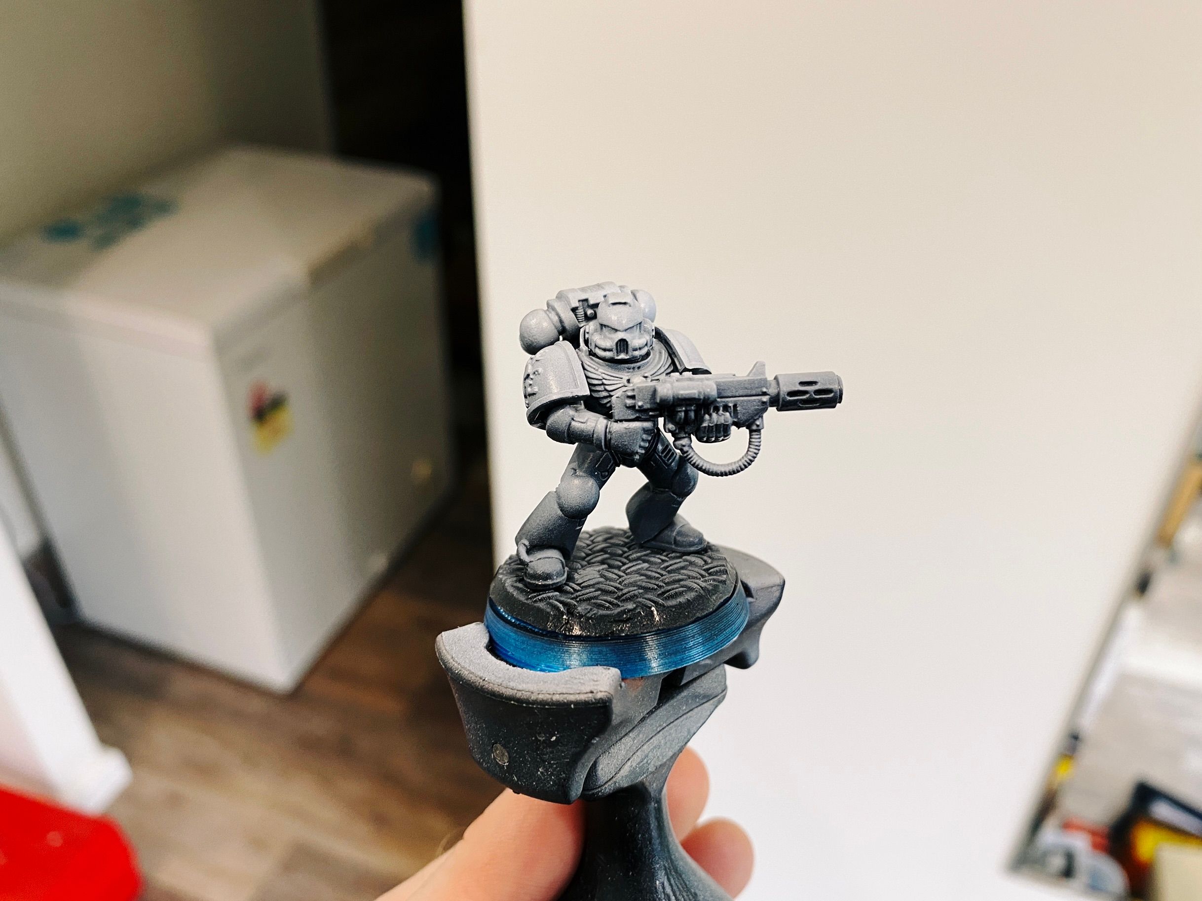 A photo of a Warhammer 40,000 Space Marine, a big heavily-armoured warrior holding a big gun, that's been undercoated in black and has a zenithal highlight of white done from the angles on the top so it looks like the light is shining on him from above. The gradient is smoooooth.