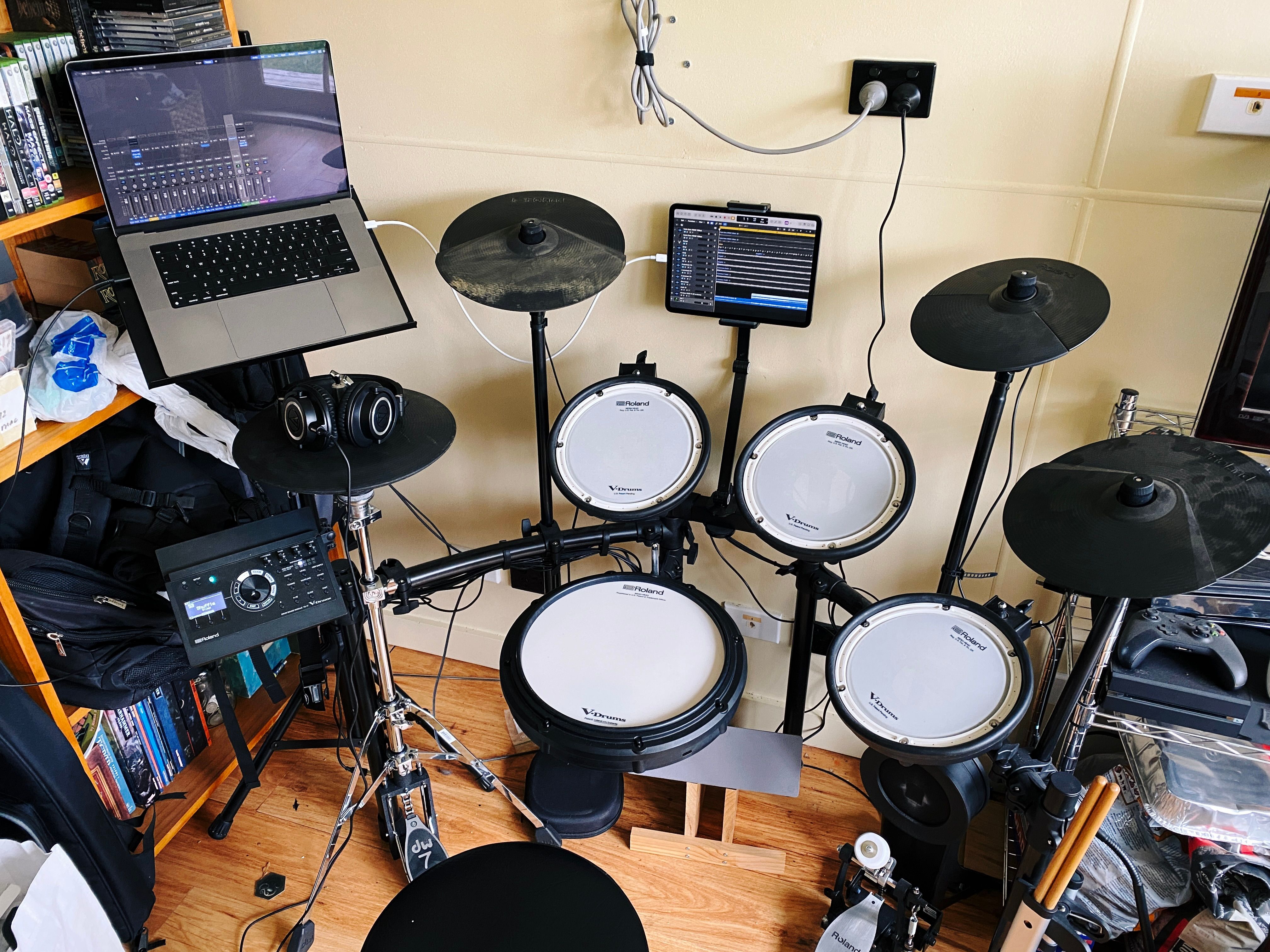 A photo of my Roland V-Drums electronic drum kit with my laptop open on a stand behind and to the left of the kit and my iPad being used as a second display for the laptop on the stand in the middle of the drum kit between the cymbals so I can see where in the song I am without needing to look awkwardly over to the left.