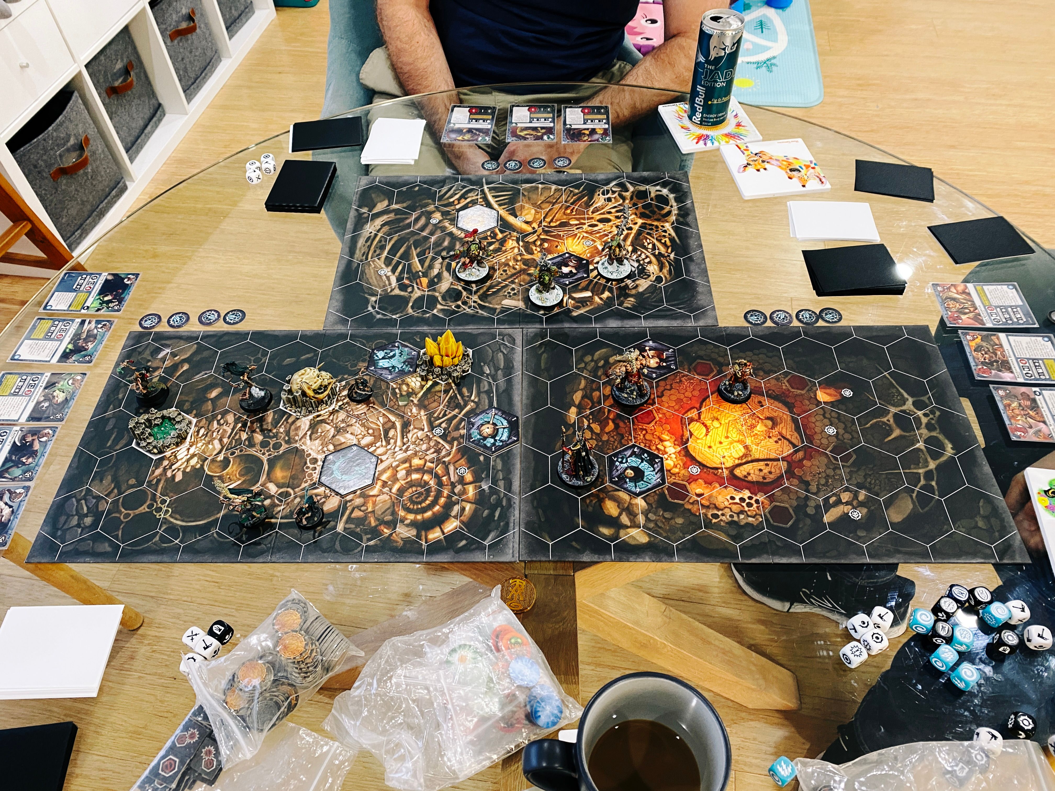 A photo of a three-player game of Warhammer Underworlds. There's three rectangular boards with hex tiles on them in an inverted-T shape, the art on the boards looks like the inside of a cave. At the left are the five Skaven ratmen of Skittershank's Clawpack, at the right are the three heavily armoured human(ish) warriors of the Gorechosen, and at the top are three heavily armoured green orks.