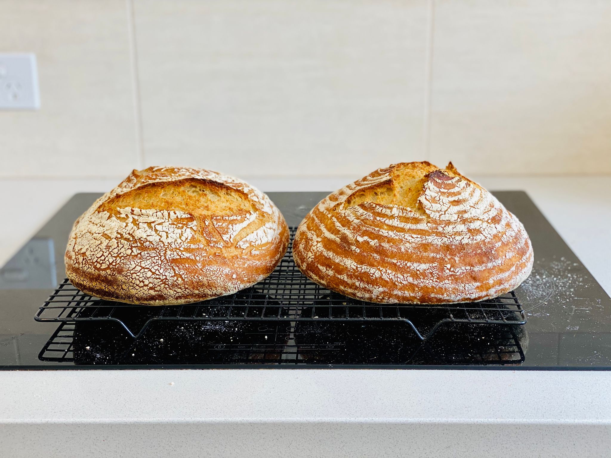 A photo of two round golden brown loaves of bread sitting on a cooling rack.