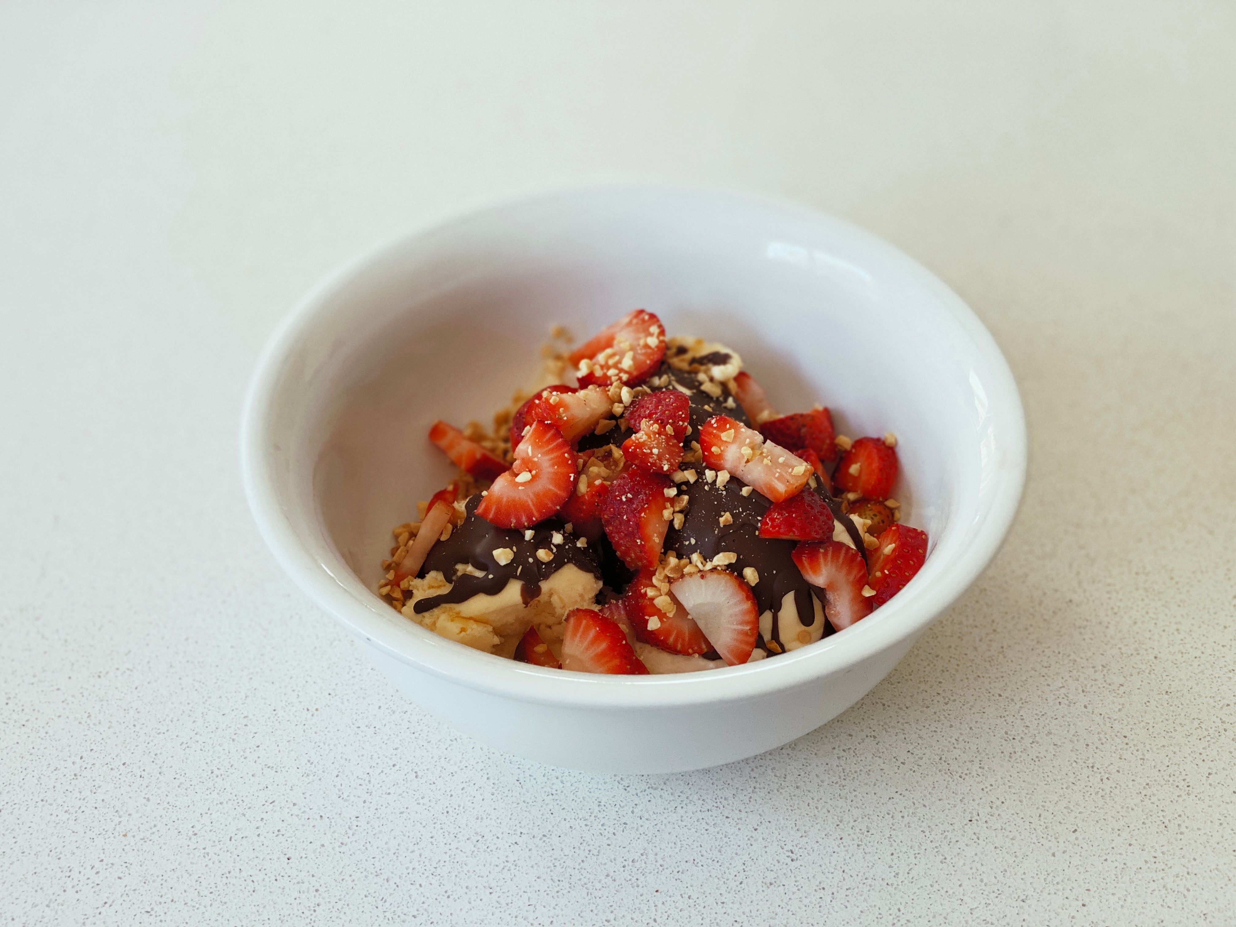 A photo of a bowl of vanilla ice cream with Ice Magic on top, and top of that is a bunch of sliced-up strawberries and crushed peanuts.